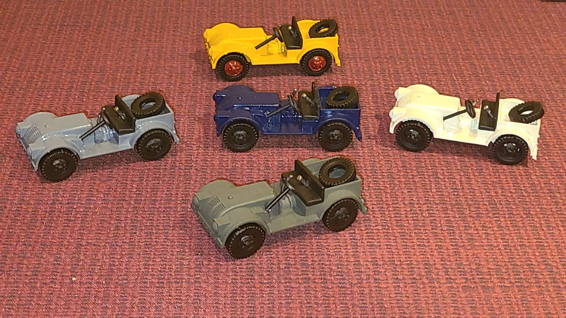 Five vintage toy cars in various colors on a red surface.