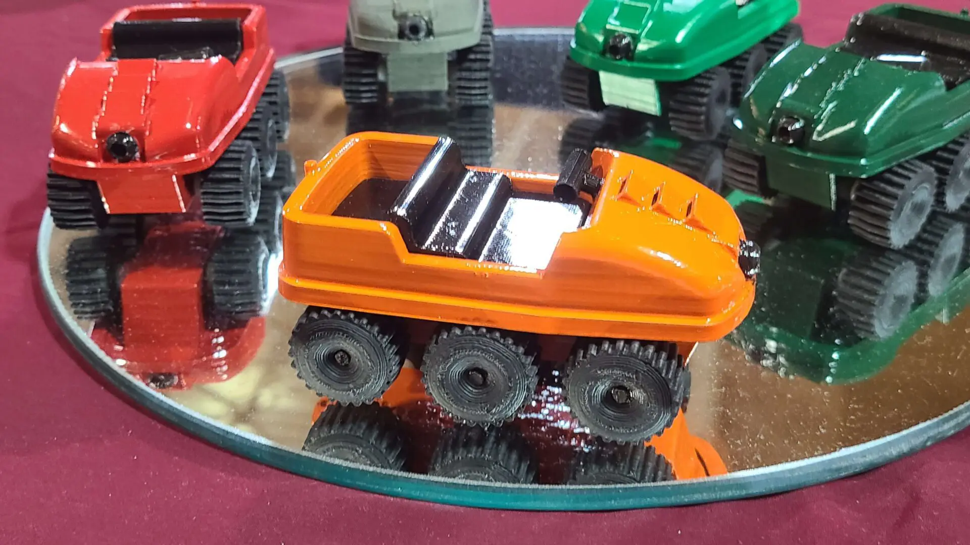An orange toy vehicle with six wheels on display.