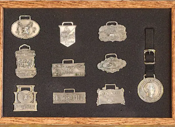 A framed collection of various silver luggage tags and medallions.