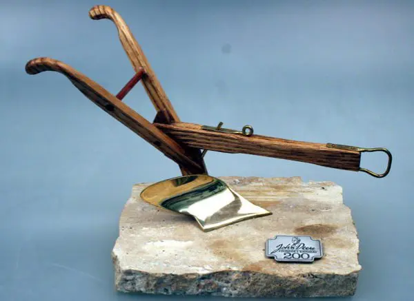 Antique wooden plow on a stone base with a nameplate.