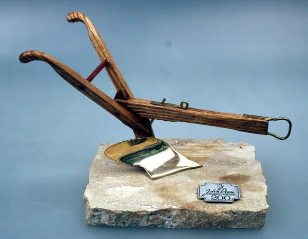 A rustic wooden plow model mounted on a stone base with a small plaque.