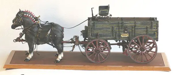 Model of a horse pulling a wooden wagon with metal wheels.
