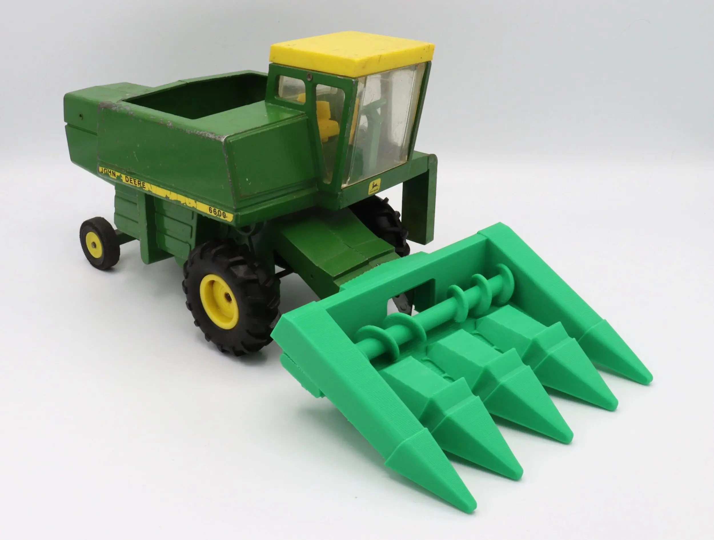 A toy green and yellow farm harvester with a green attachment.