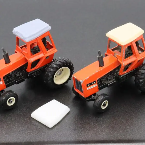 Two orange model tractors on a black surface with a white object between them.