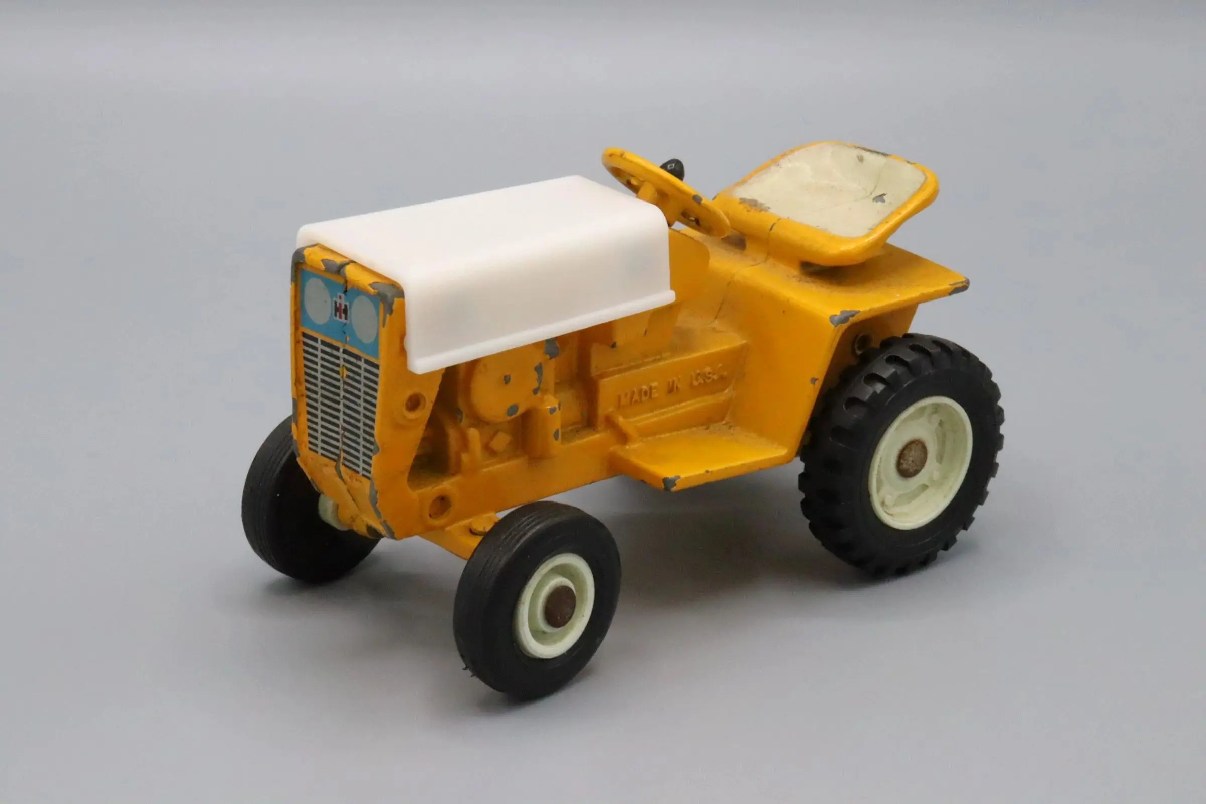 A yellow and white toy tractor with black wheels on a gray background.