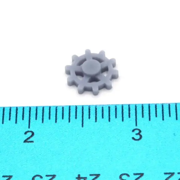 A tiny gray gear next to a ruler showing millimeter measurements.