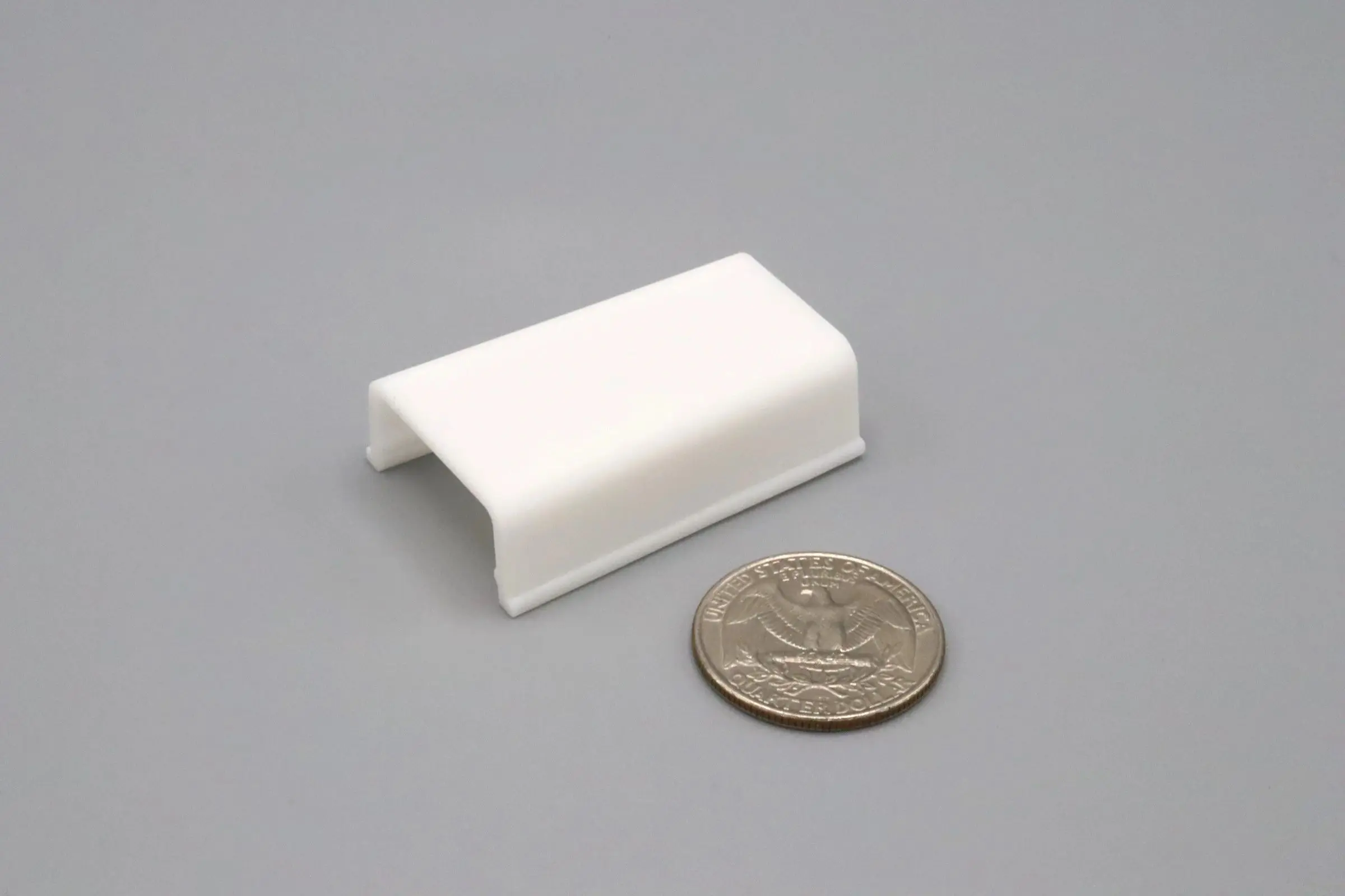 A small white plastic clip next to a quarter for size comparison.