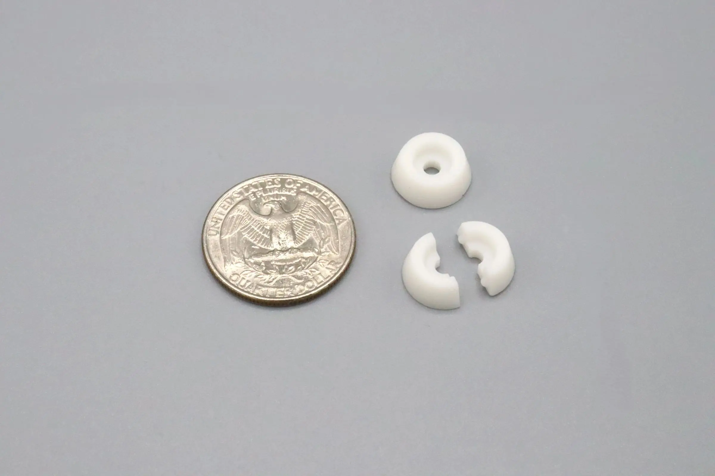 A quarter next to two whole and one broken small white plastic rings.