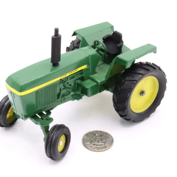 A small green toy tractor with yellow wheels next to a coin for scale.