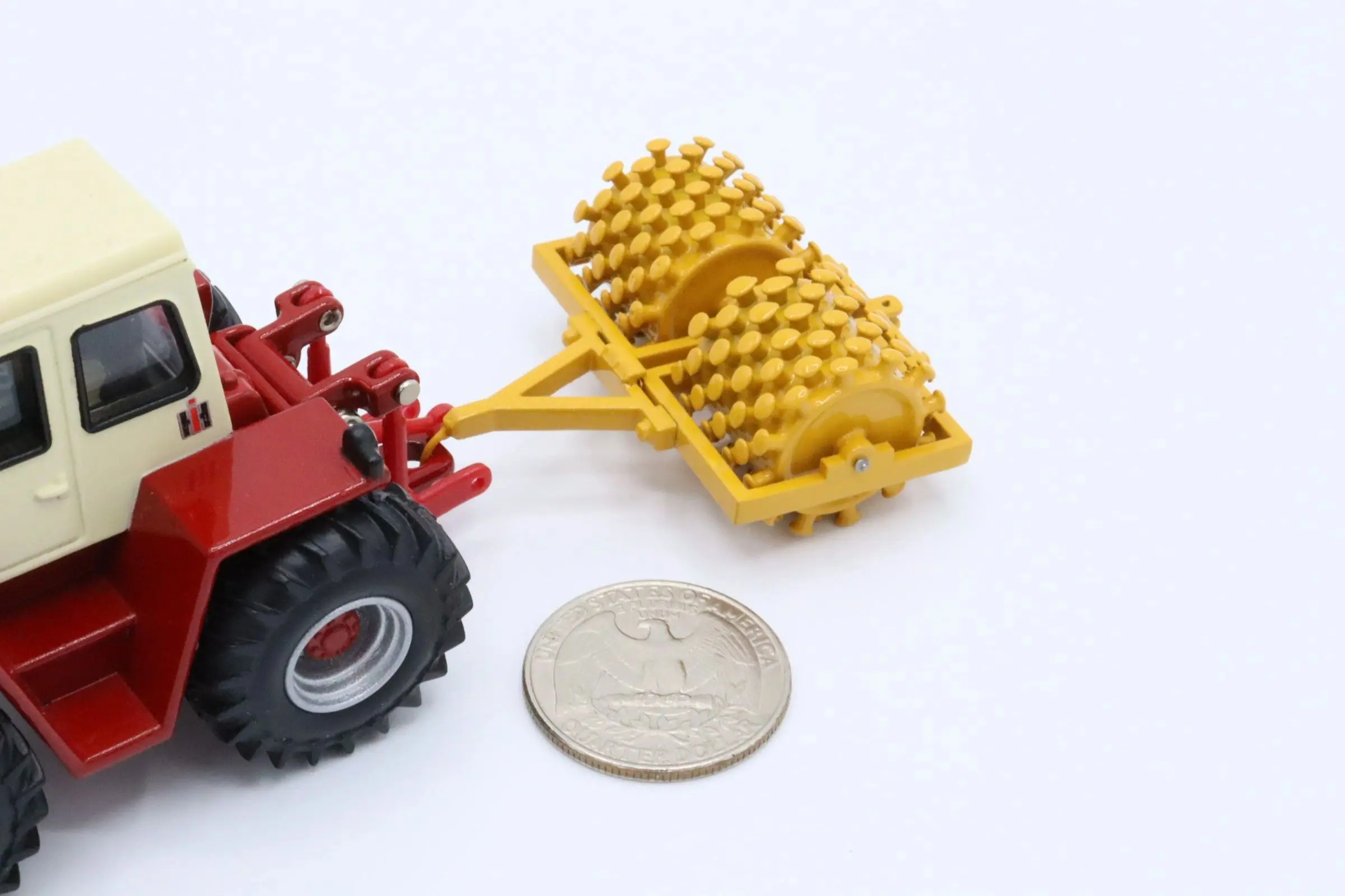 A miniature red tractor attached to a yellow roller next to a quarter for scale.