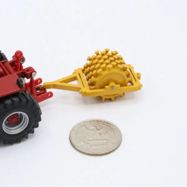 A small red toy tractor with a yellow trailer next to a coin for scale.