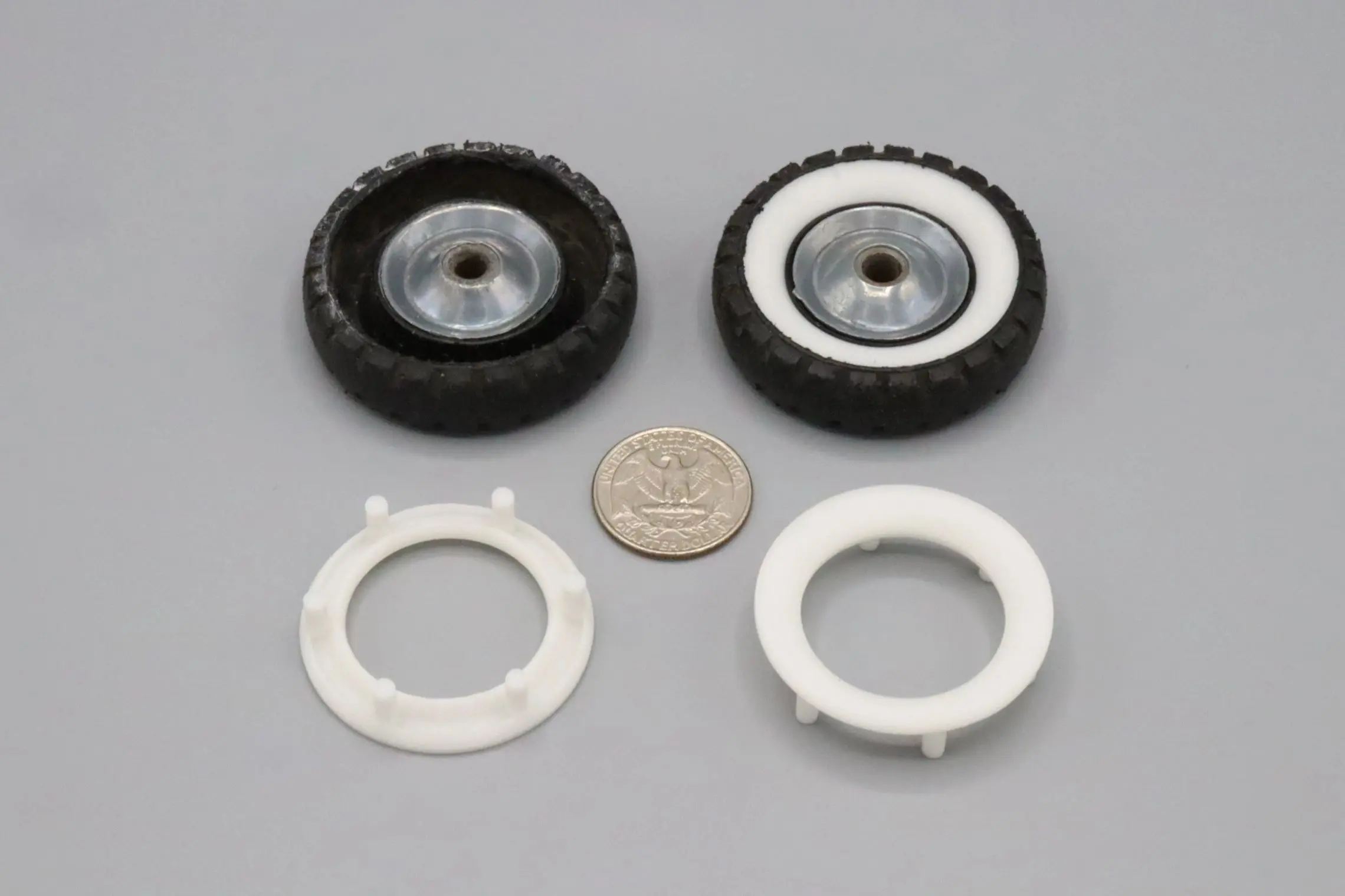 Two small wheels with white plastic rims and a coin for scale.