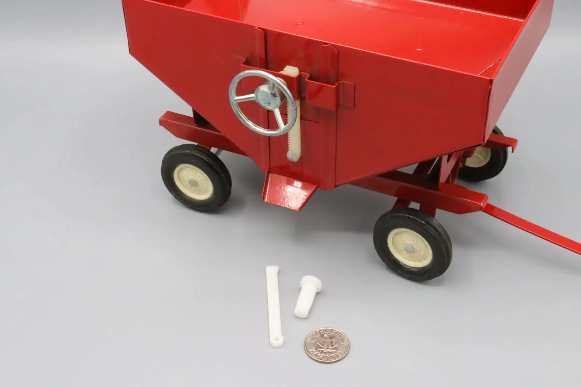 Red wagon with white wheels and small plastic parts beside a coin.