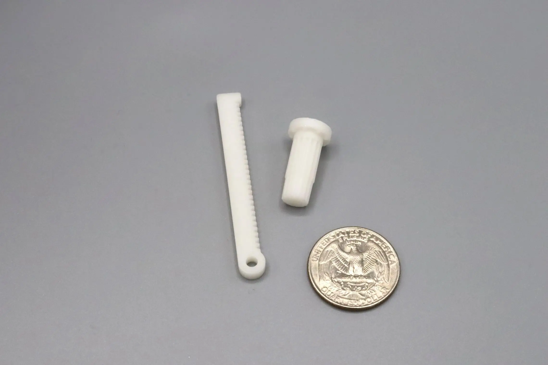Two small white plastic parts beside a quarter for scale.