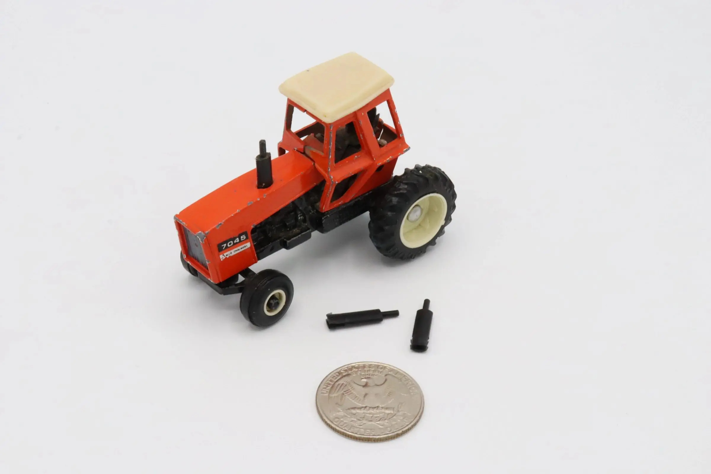 A small orange toy tractor with black exhaust pipes and a coin for scale.