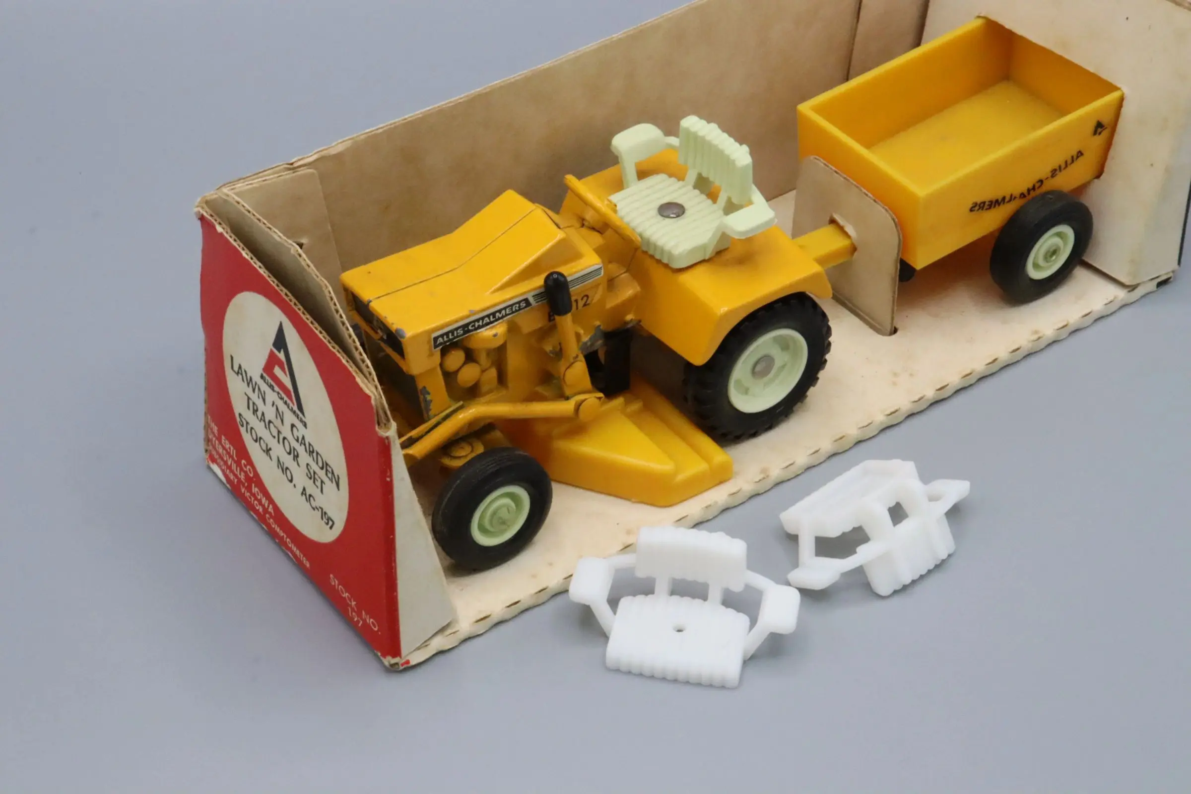 Vintage toy tractor with detachable parts and yellow trailer in original box.