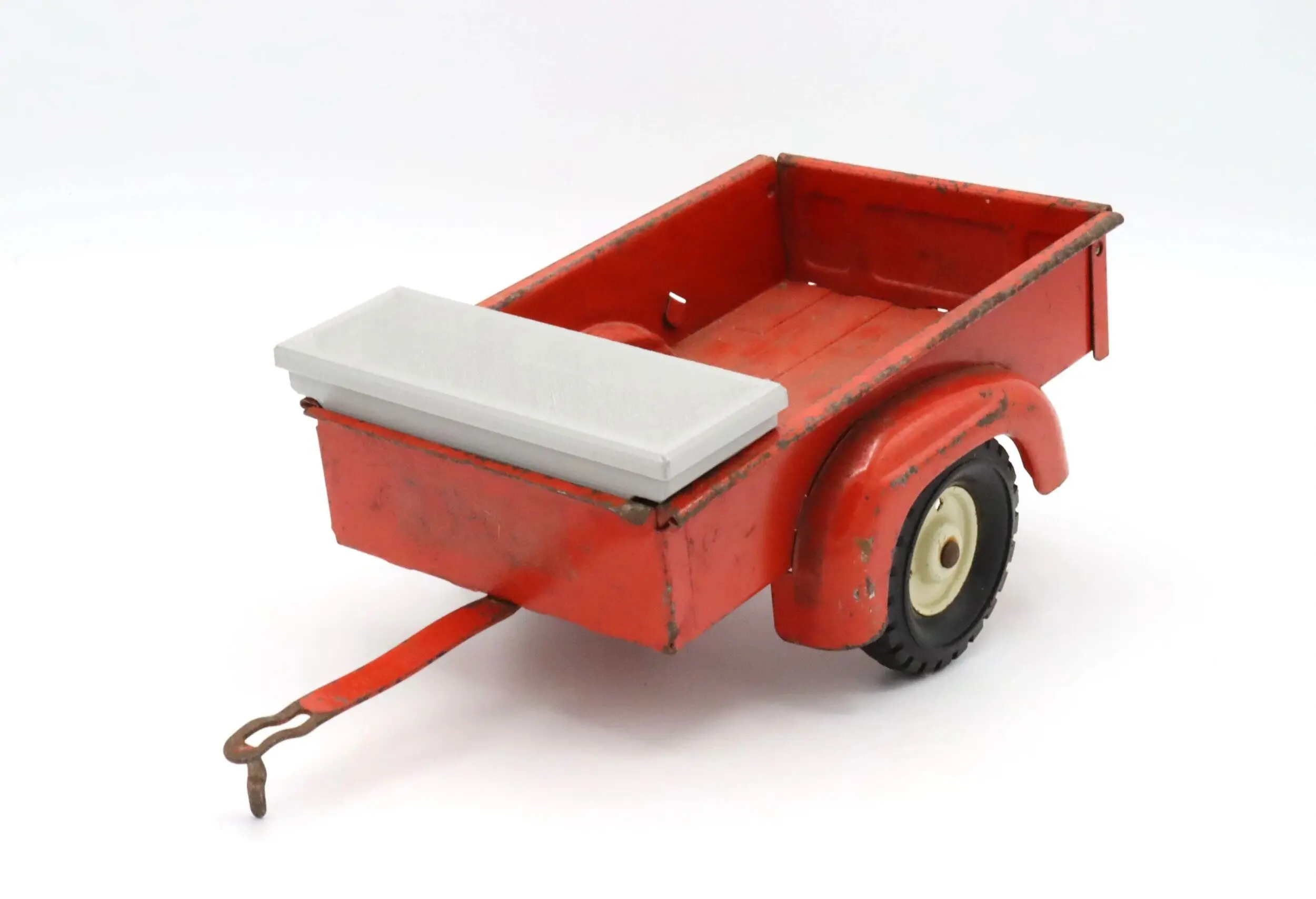 Red metal trailer with a single axle and white cushioned top on the front.