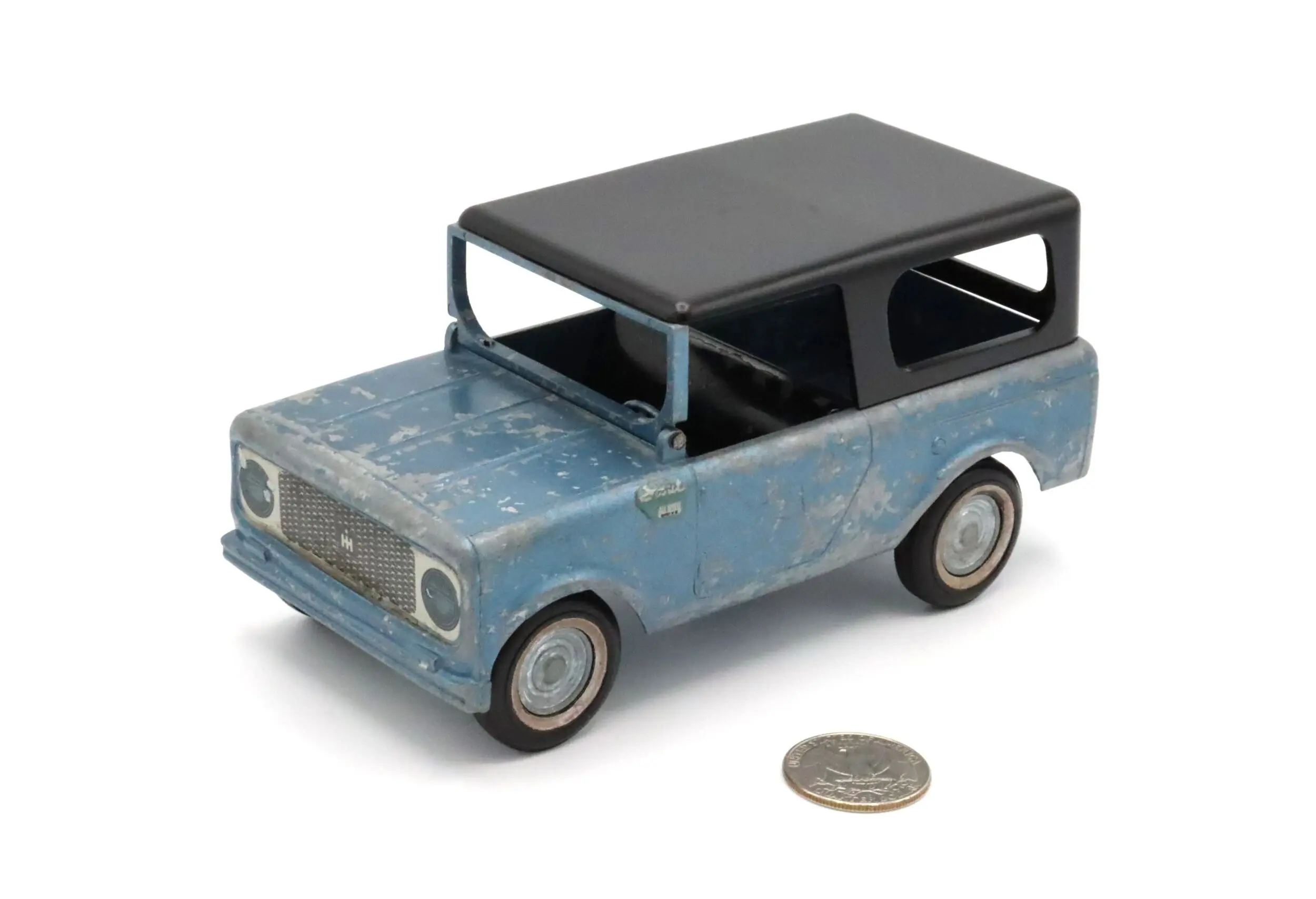 A vintage blue toy car with a black roof beside a coin.