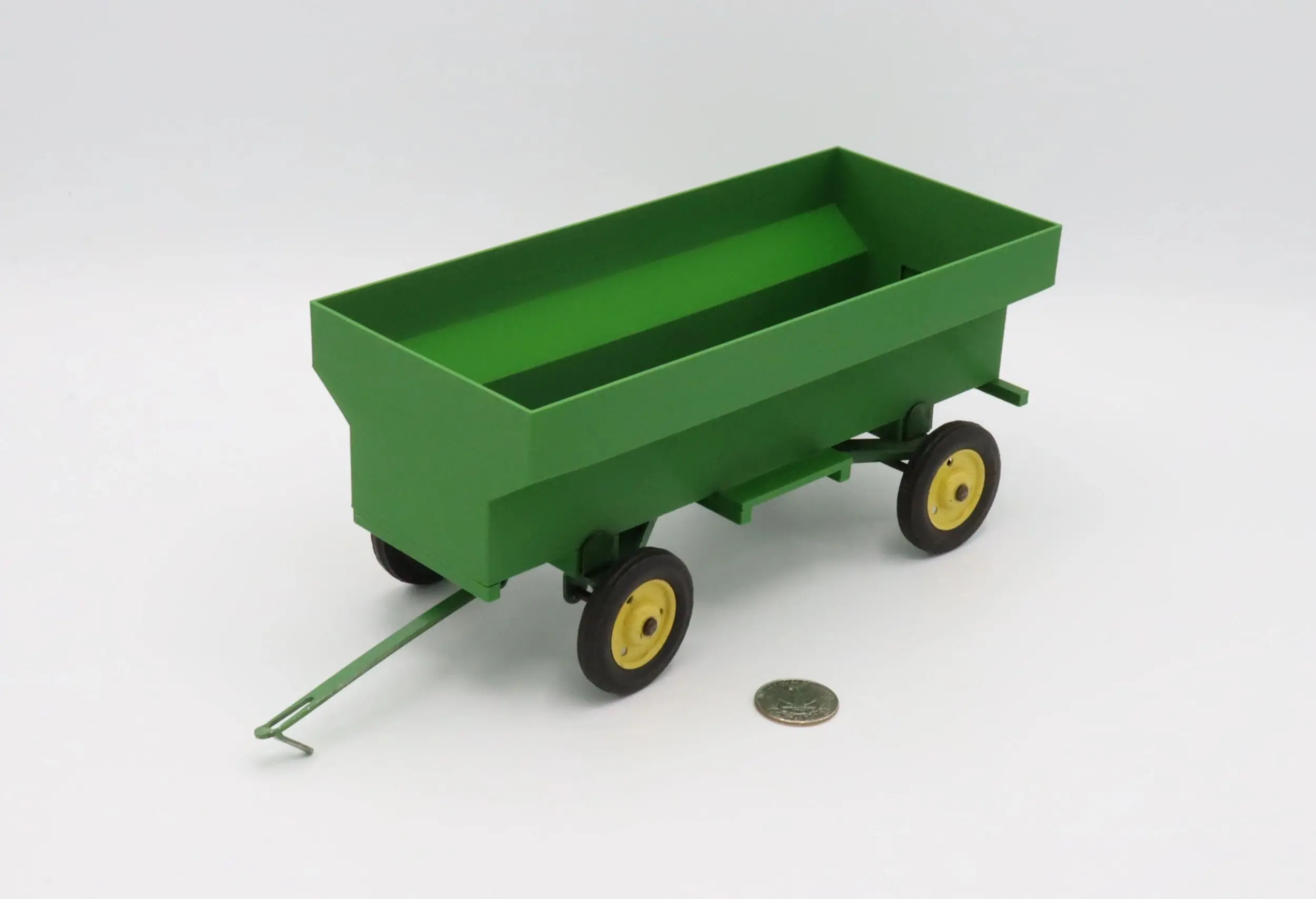 Green toy wagon with yellow wheels and a handle, next to a coin for scale.
