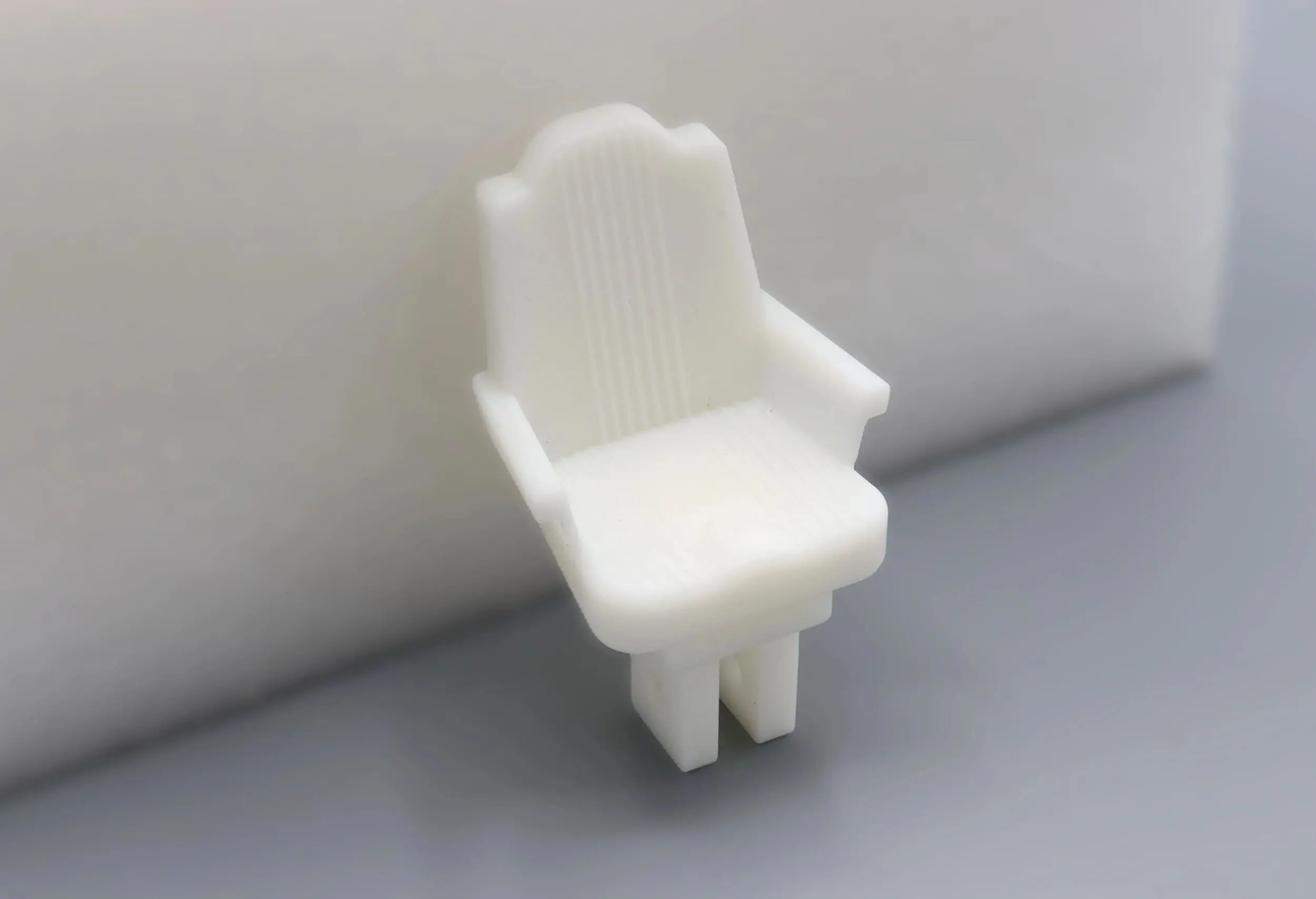 A small white plastic chair with armrests on a gray surface.