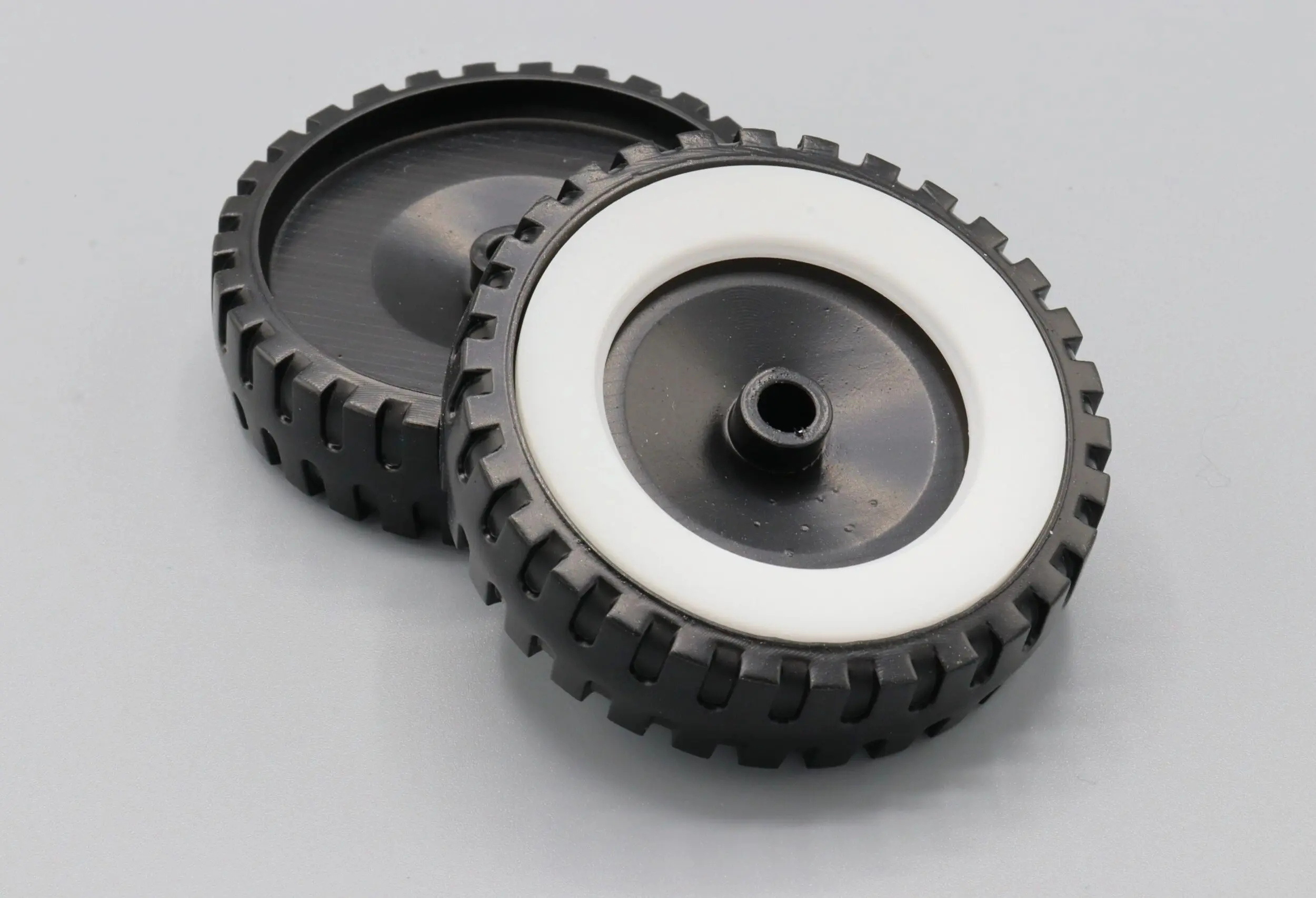 Two small black rubber wheels with white rims on a grey surface.