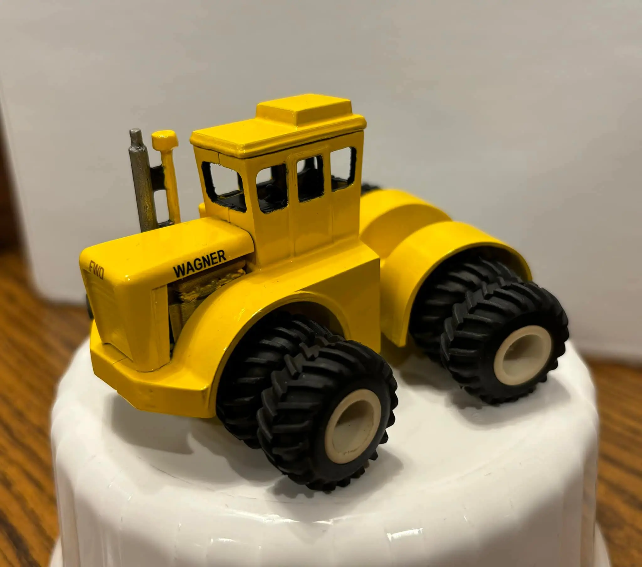 Yellow toy tractor with large black wheels on white surface.