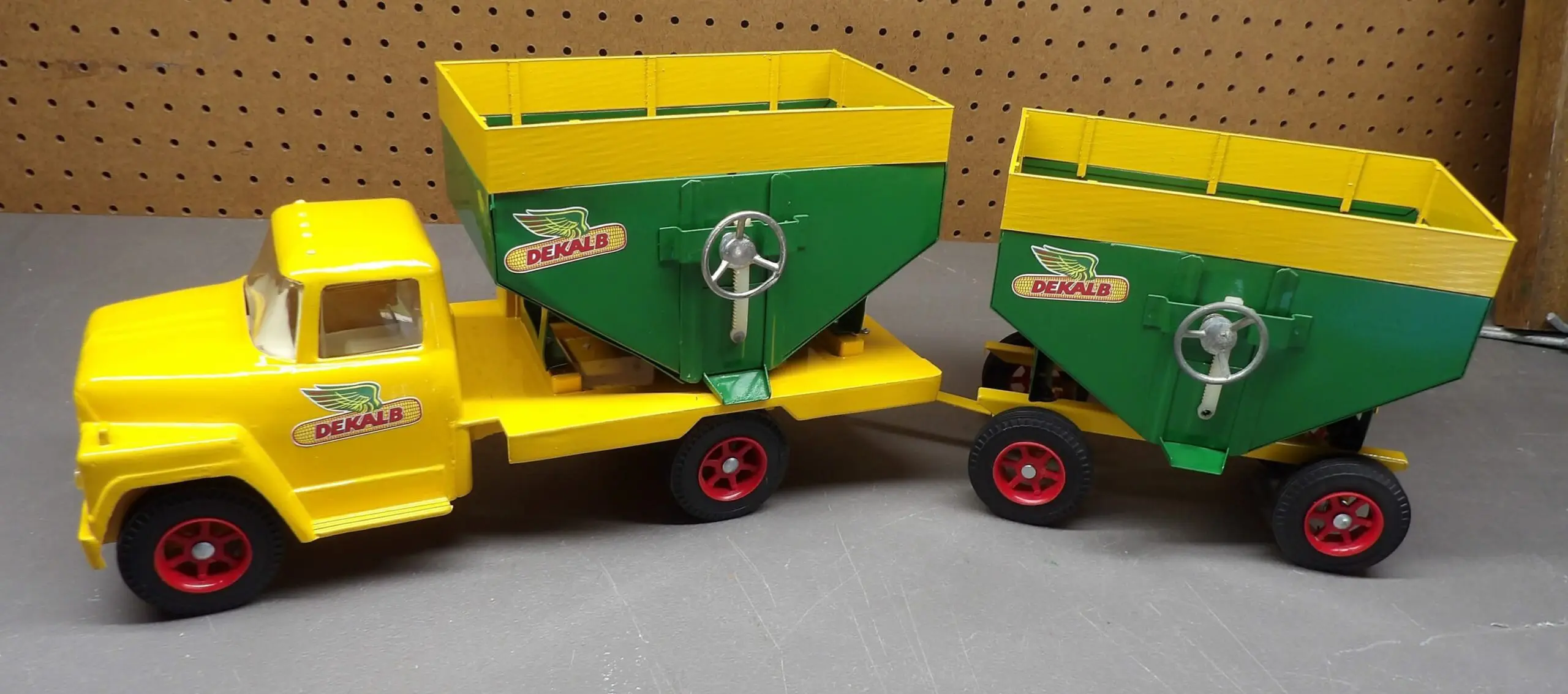 Vintage yellow and green toy grain spreader with red wheels.