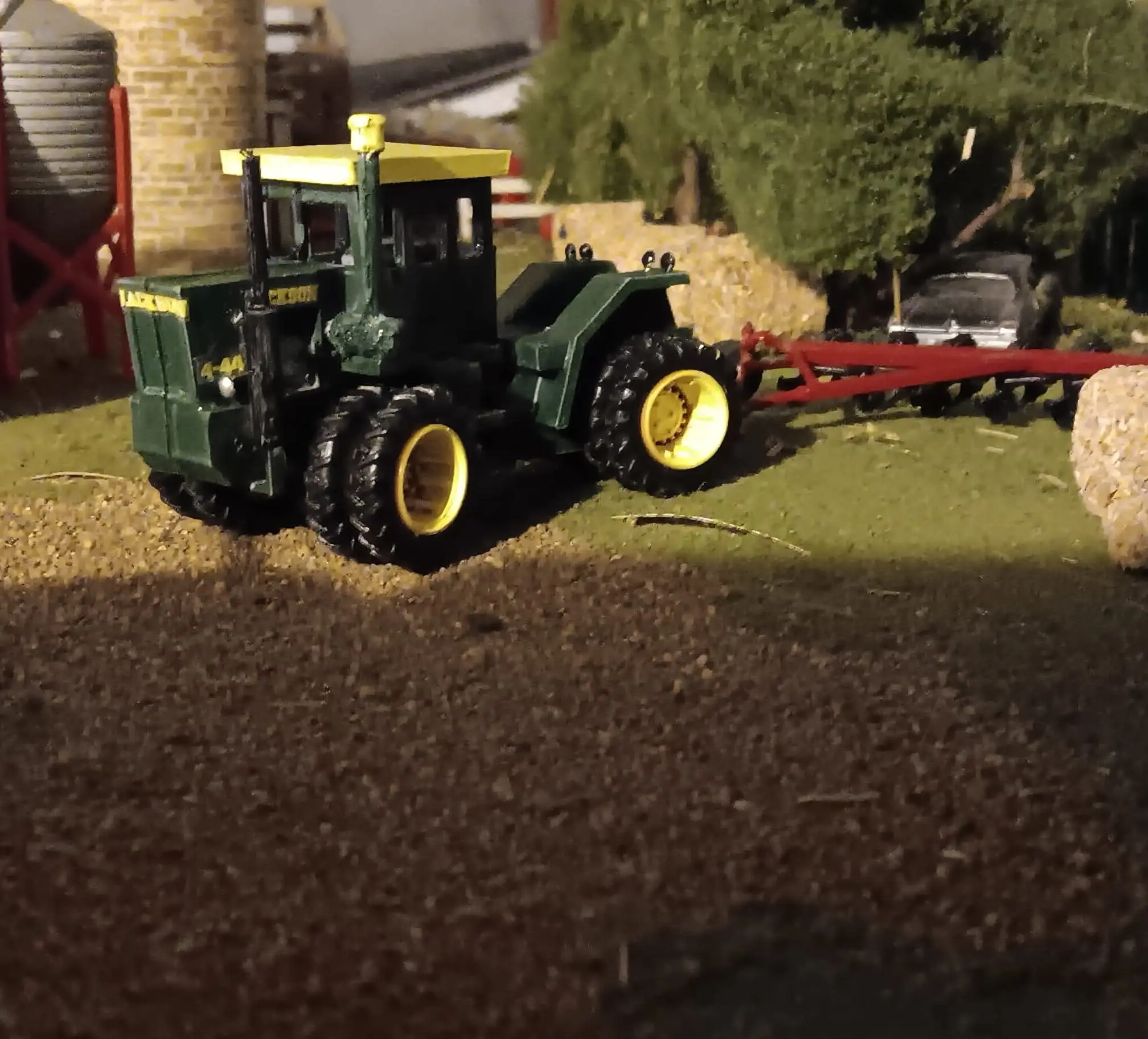 A green tractor pulling a red farming trailer in a rural setting.