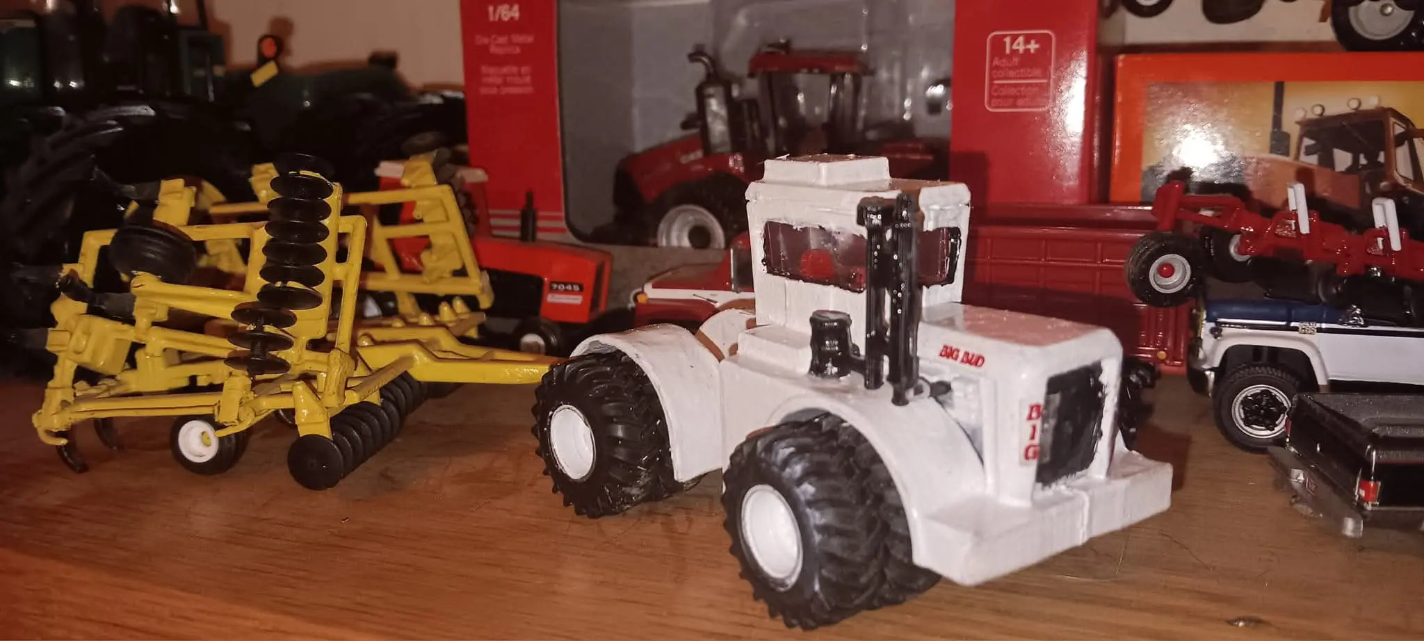 A white toy tractor with large wheels on a wooden surface.