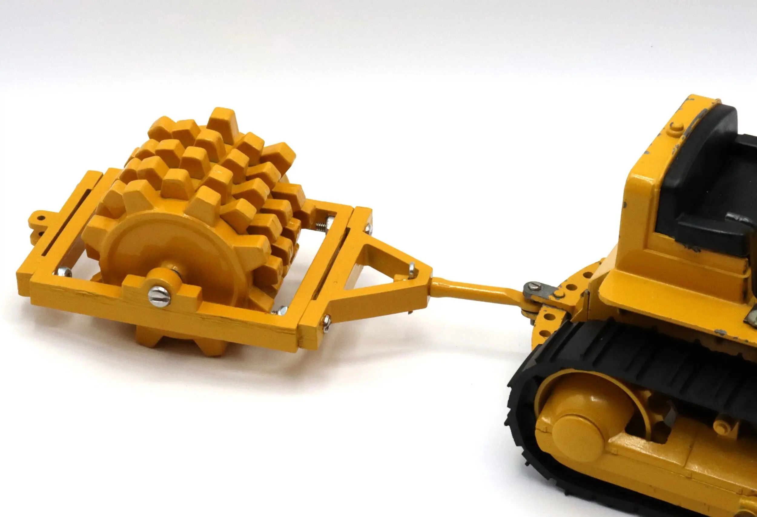 A yellow toy bulldozer with a roller attachment on a white background.