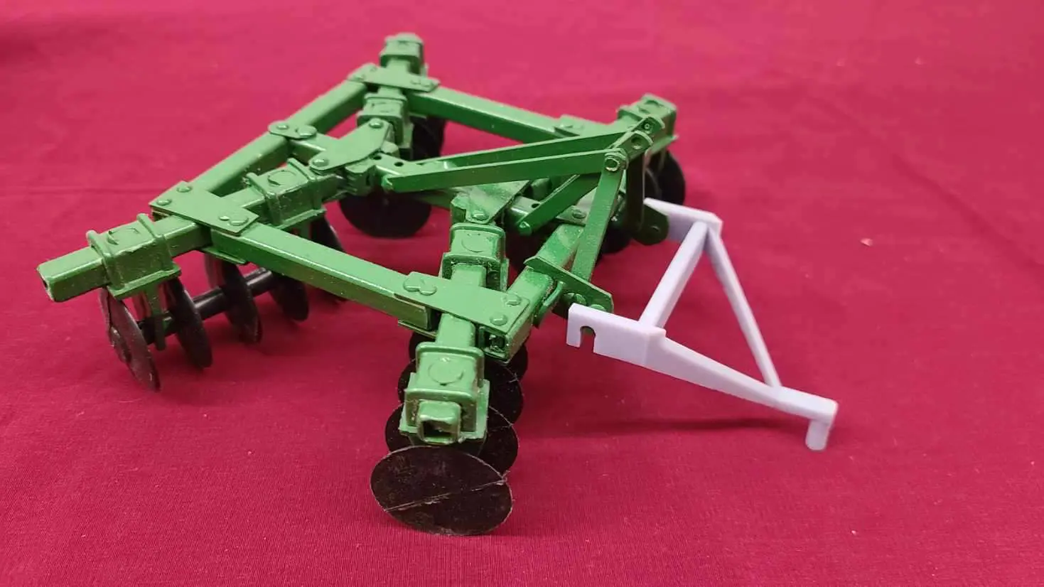 Green and white toy tractor attachment against a red background.