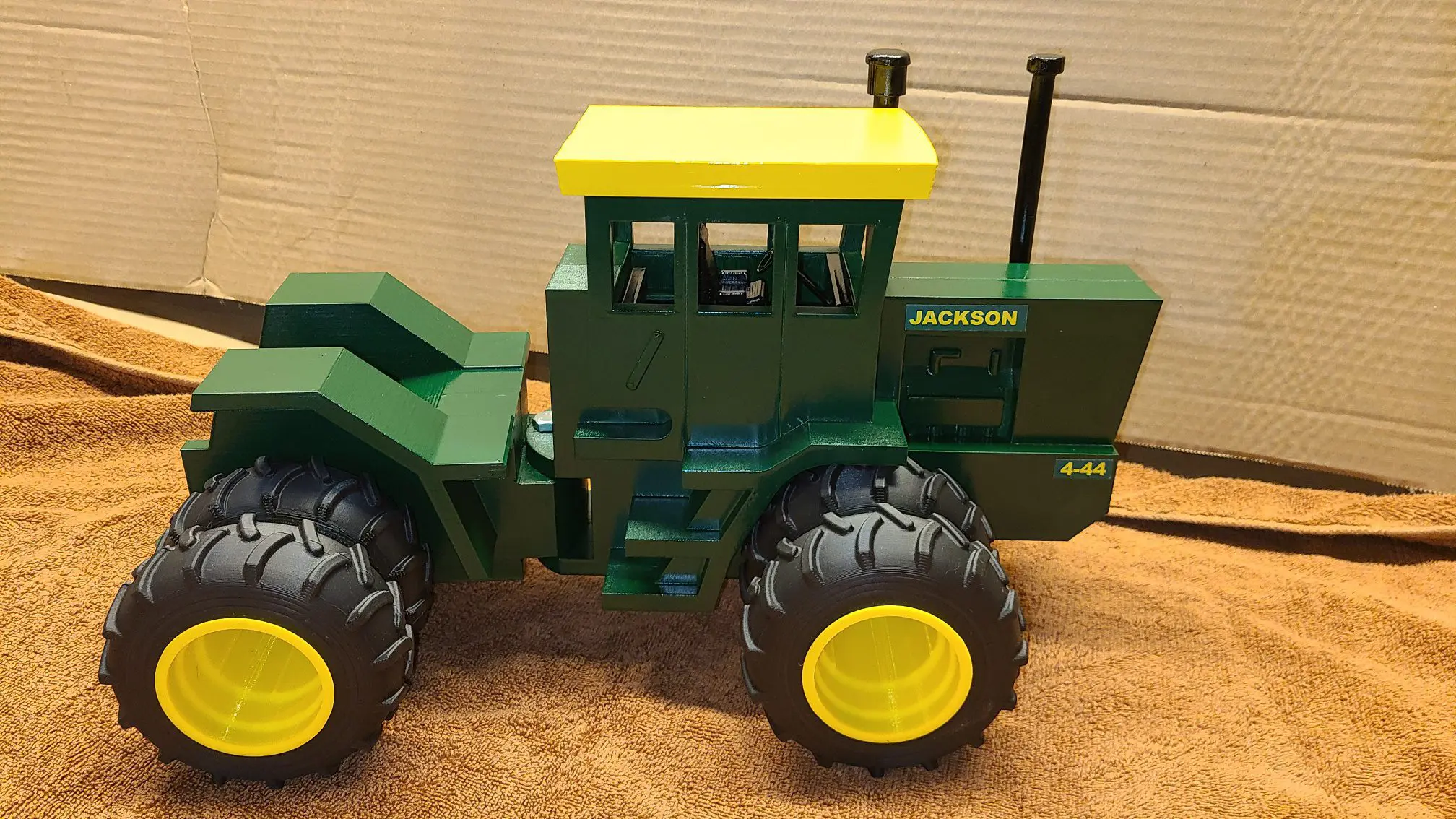 A green and yellow toy tractor with large wheels on a wooden surface.