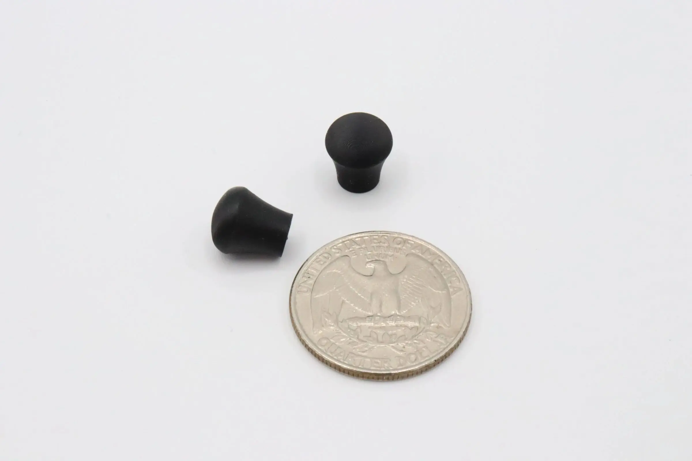 Two small black rubber grommets next to a coin for scale.