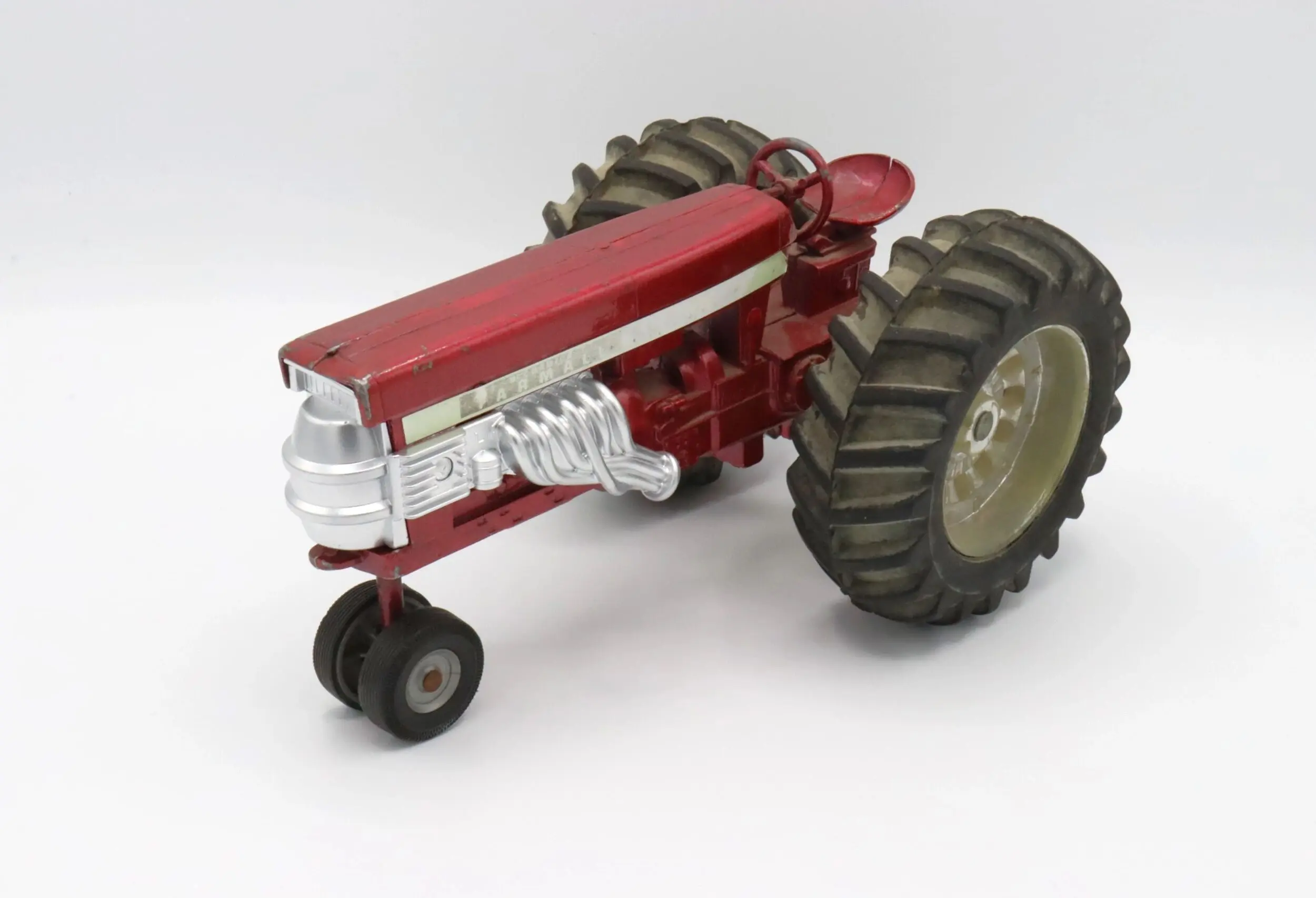 A vintage red toy tractor with large rear wheels on a white background.