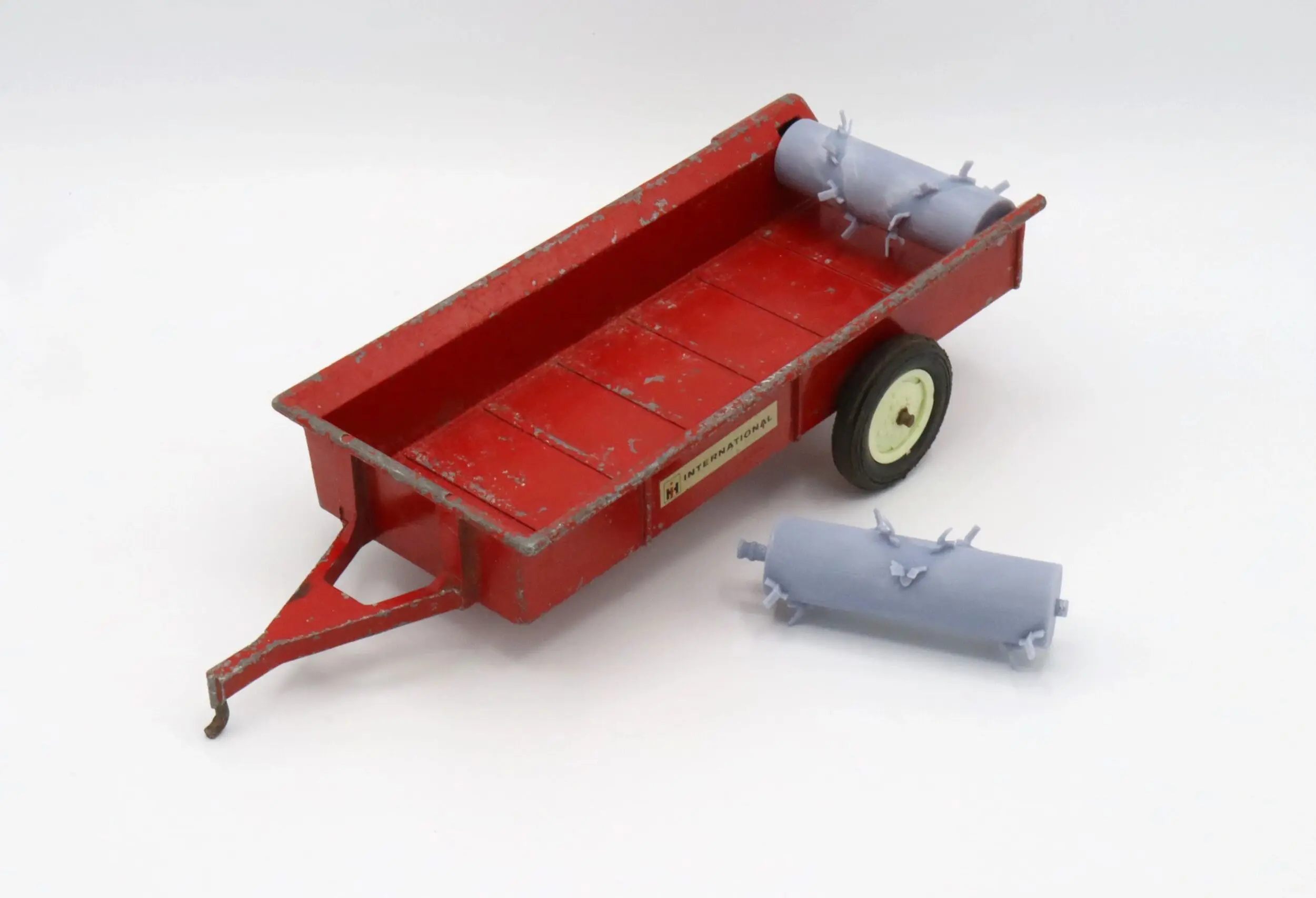 Red toy trailer with two cylindrical accessories on a white background.