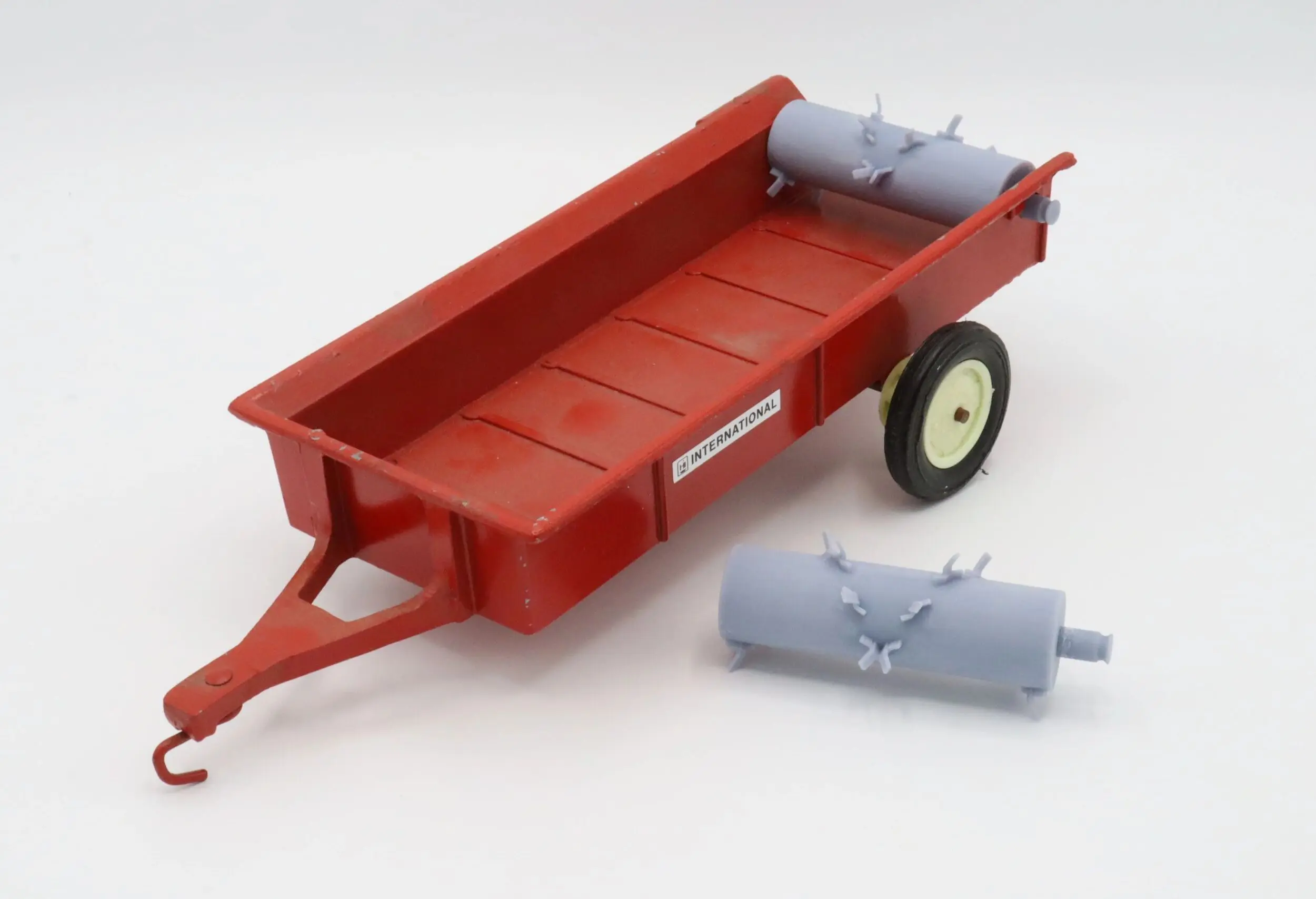 A red toy trailer with two gray cylindrical attachments on a white background.