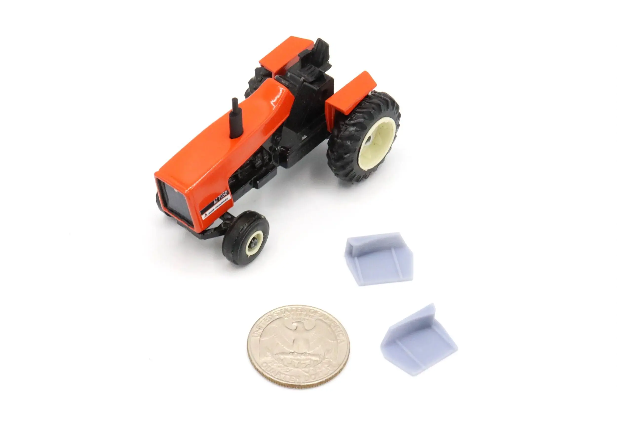 A small orange toy tractor with a coin and two miniature hay bales.