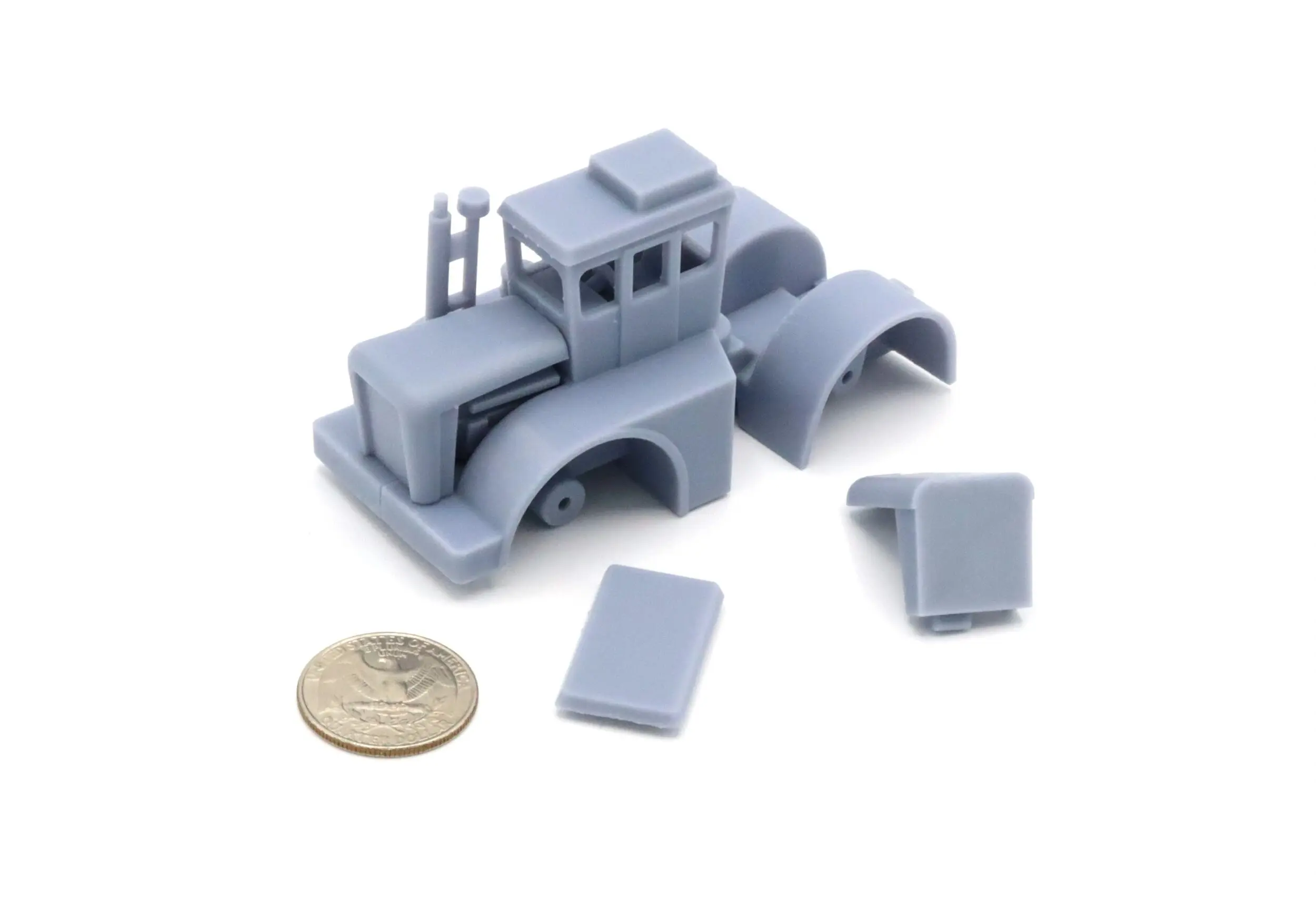 A gray model car kit with separate parts and a coin for scale.