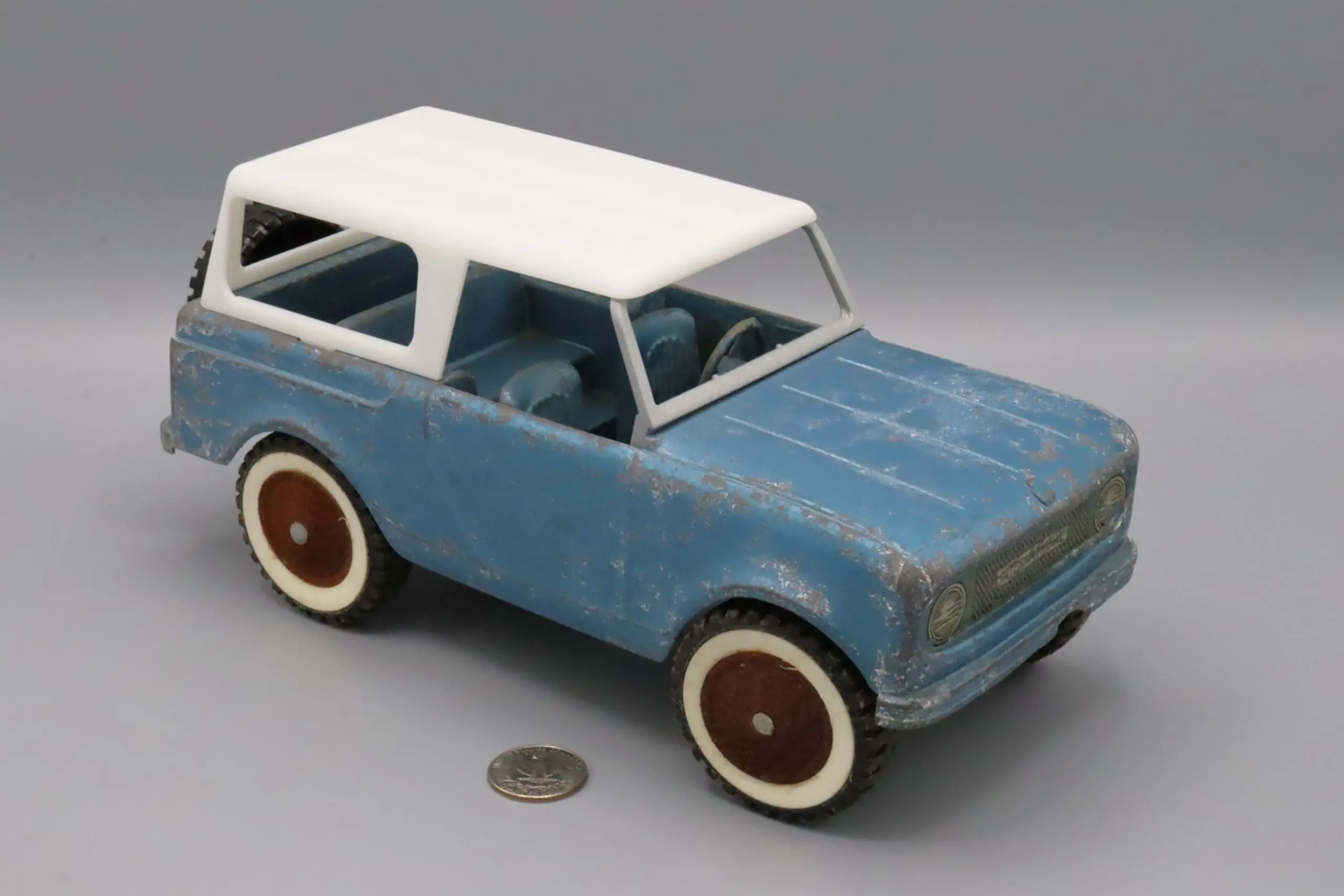 Vintage blue toy car with white roof and large wheels beside a coin.