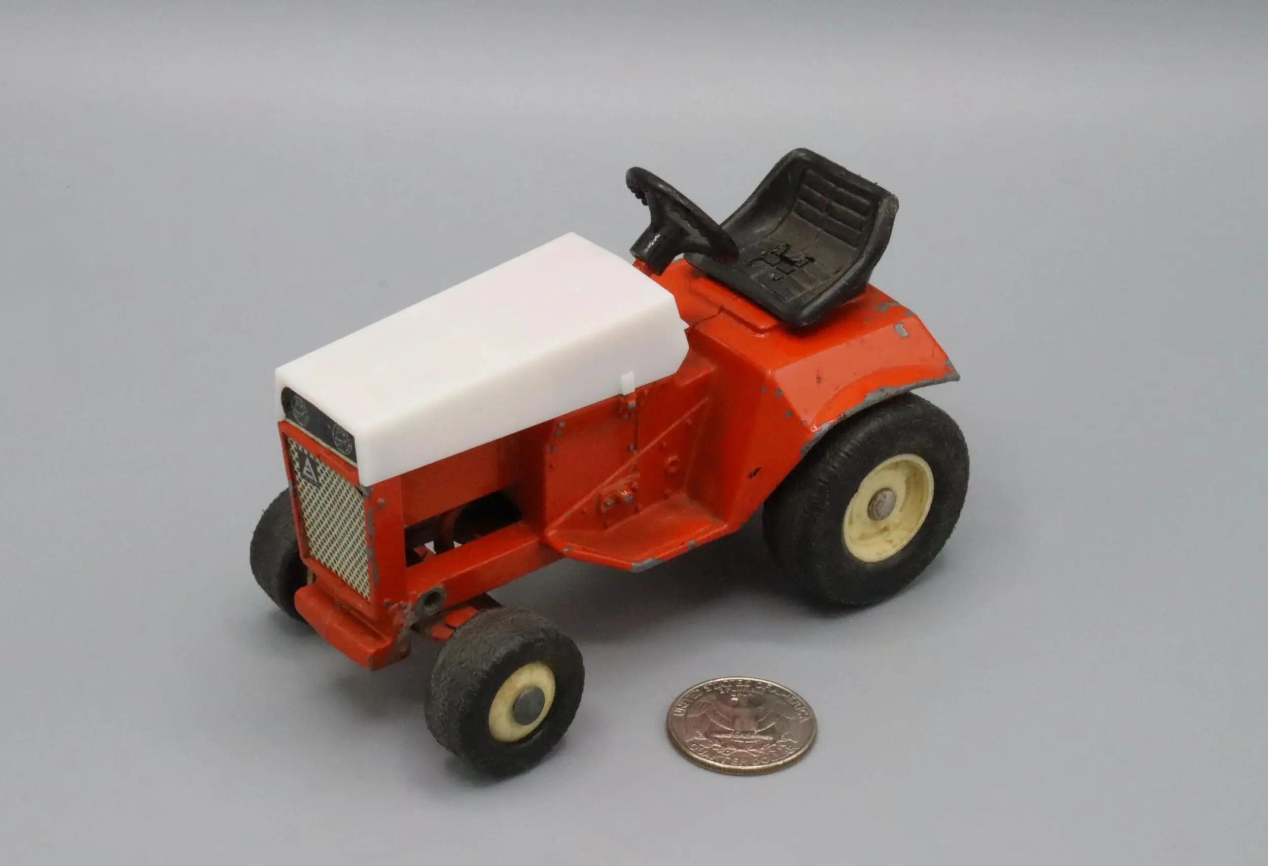 A small red and white toy tractor beside a coin for scale.
