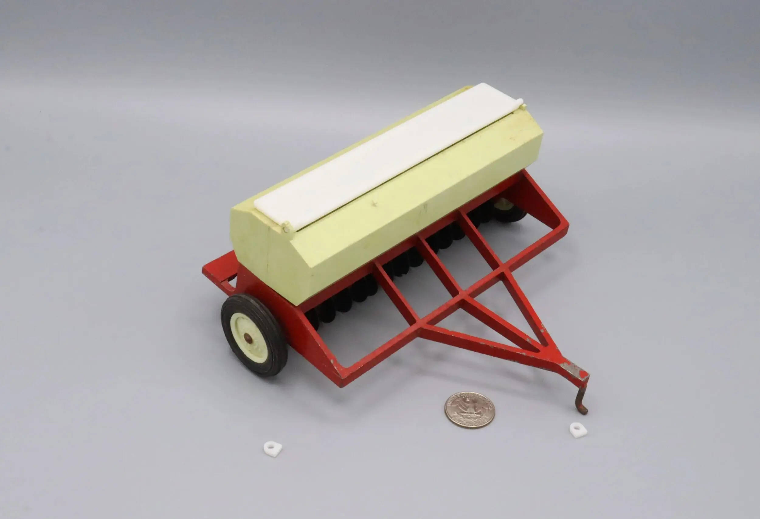 A miniature farm seed planter with a red base and yellow container.