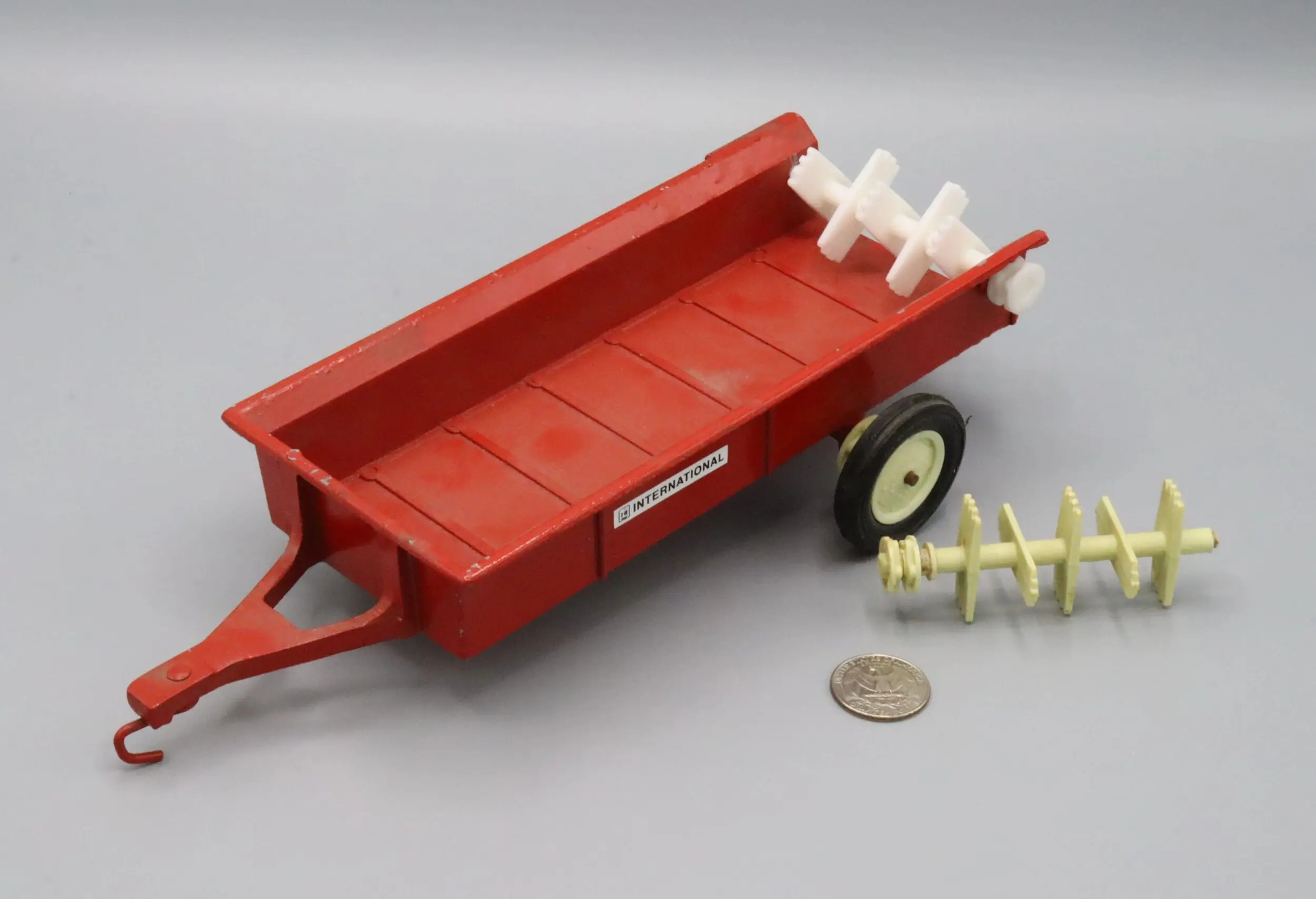 A small red toy trailer with white auger attachments and a coin for size reference.