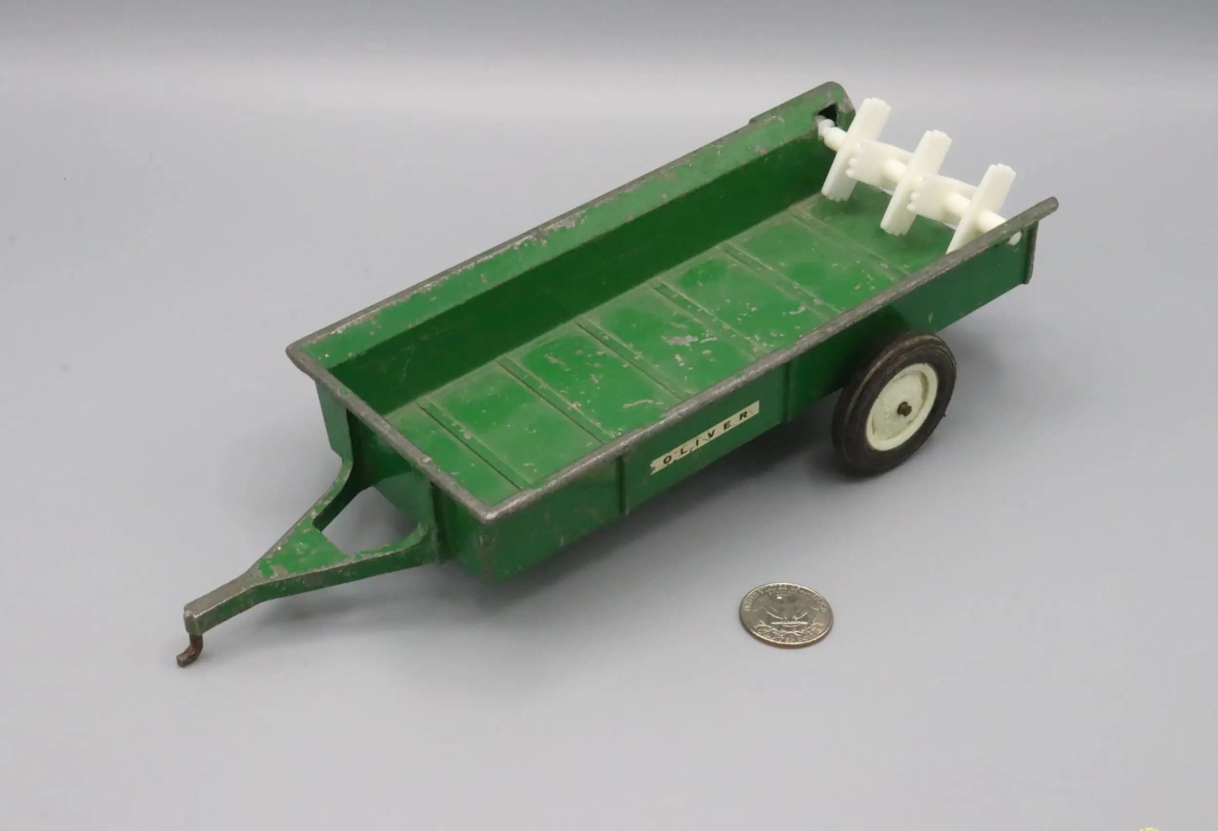 Vintage green toy trailer with white wheels and a coin for scale.