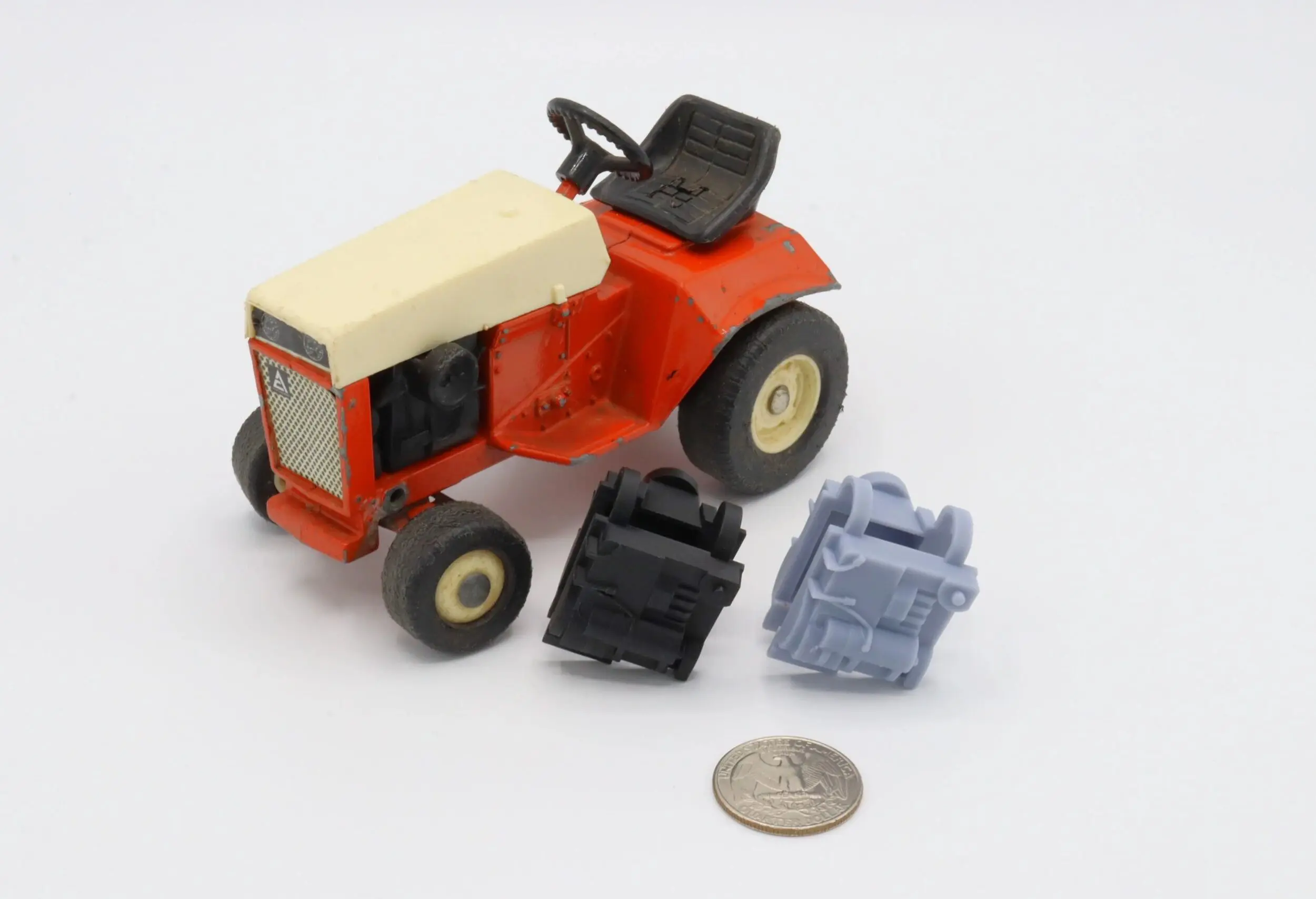 A miniature red and white tractor with two small engine models and a coin for scale.