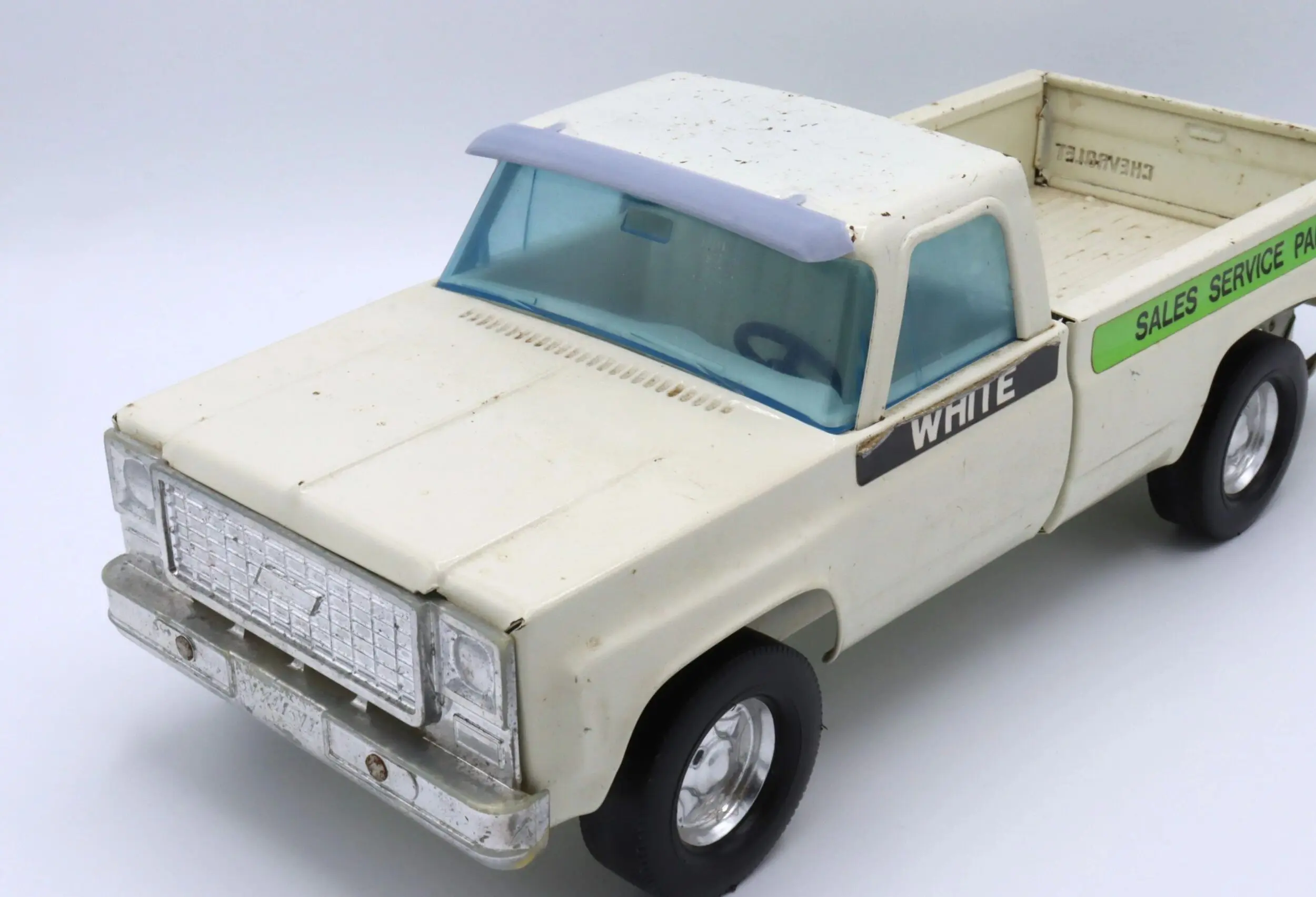 Vintage white pickup toy truck with blue windows and 'Chevrolet' decal.