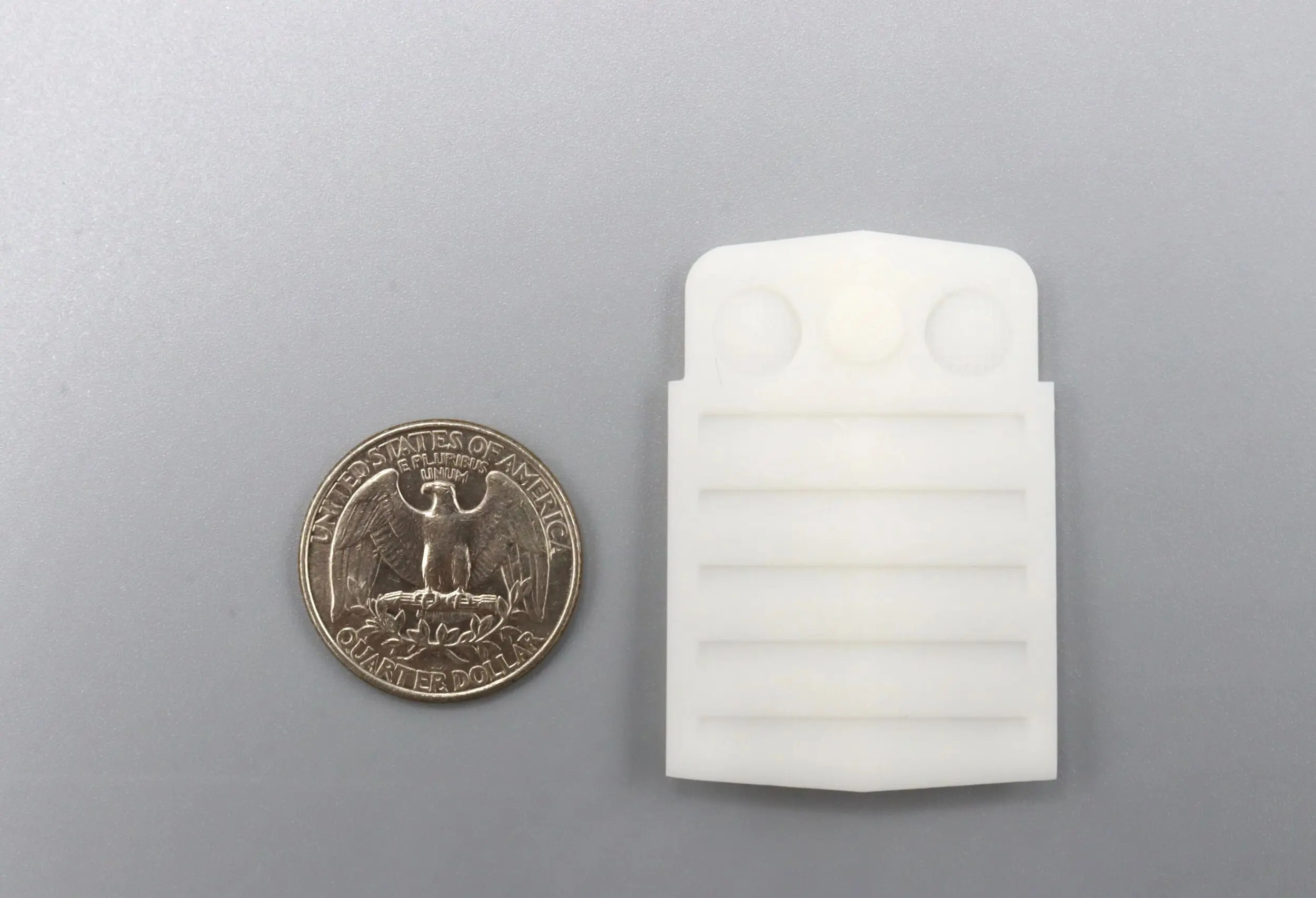 A quarter coin next to a small white plastic object with grooves.
