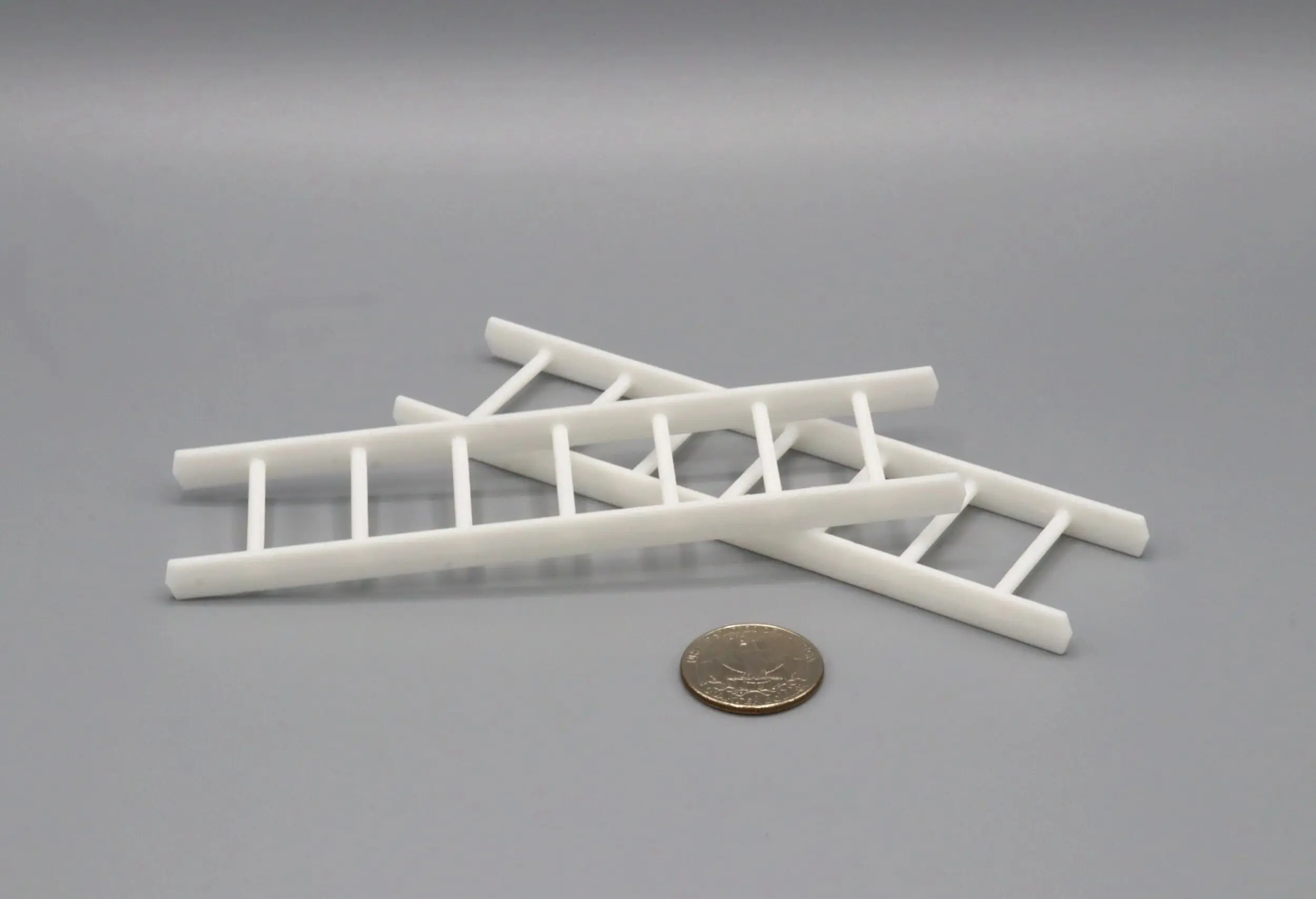 Two small white plastic ladders next to a coin for scale.