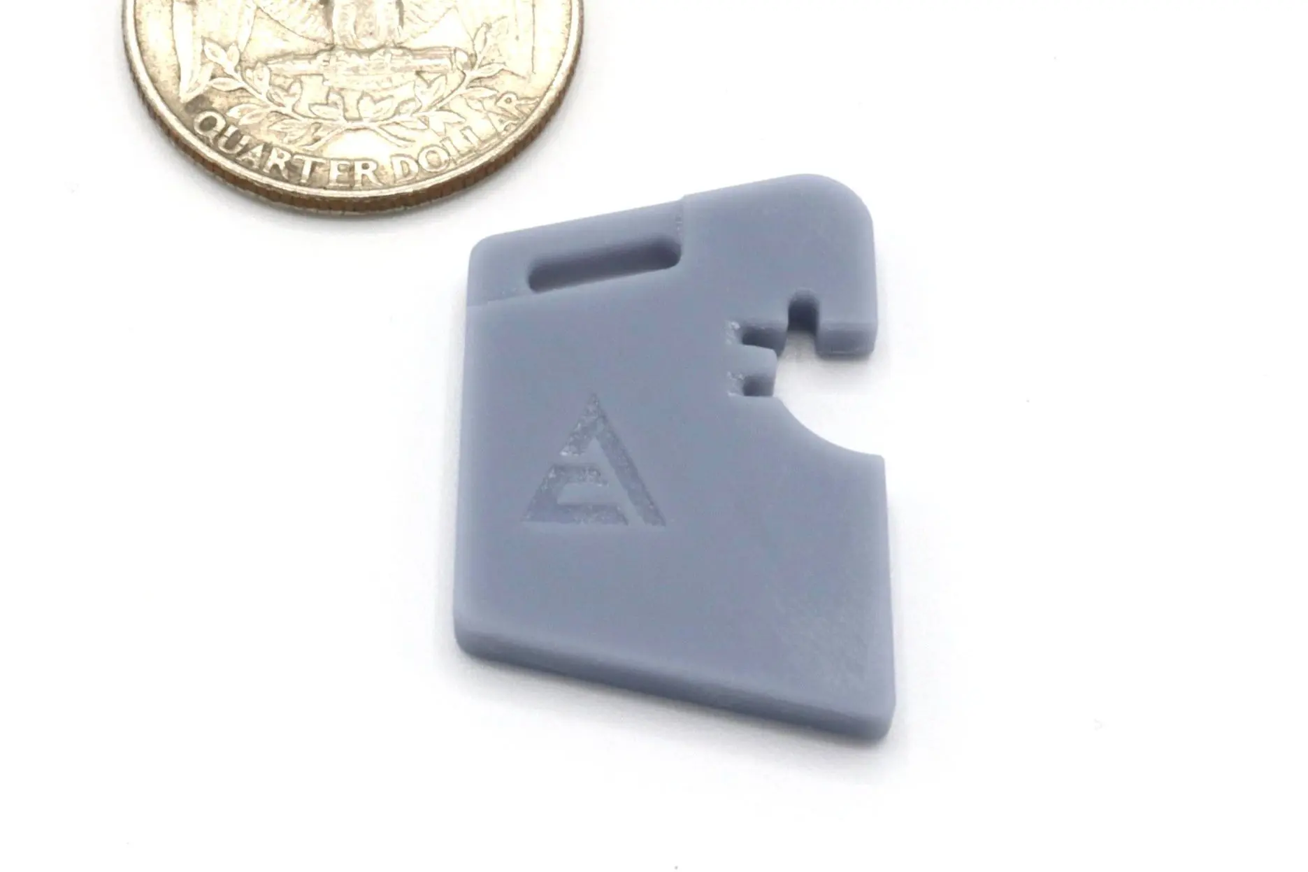 Small gray plastic clip with a triangular logo, shown next to a coin for scale.