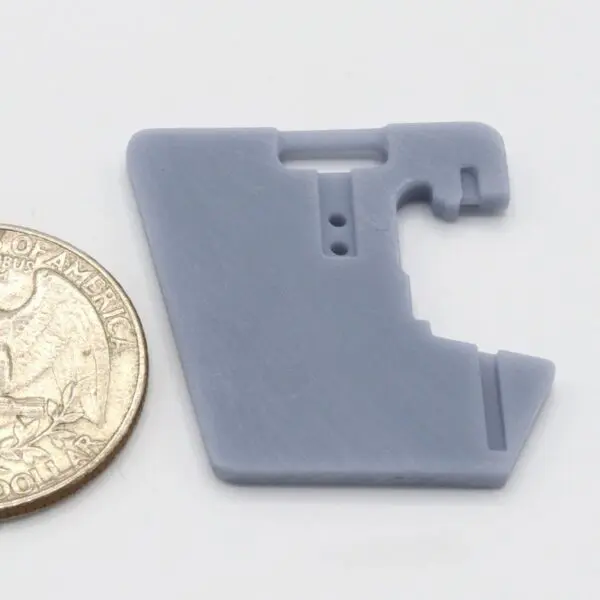 Small gray plastic part next to a quarter for size.