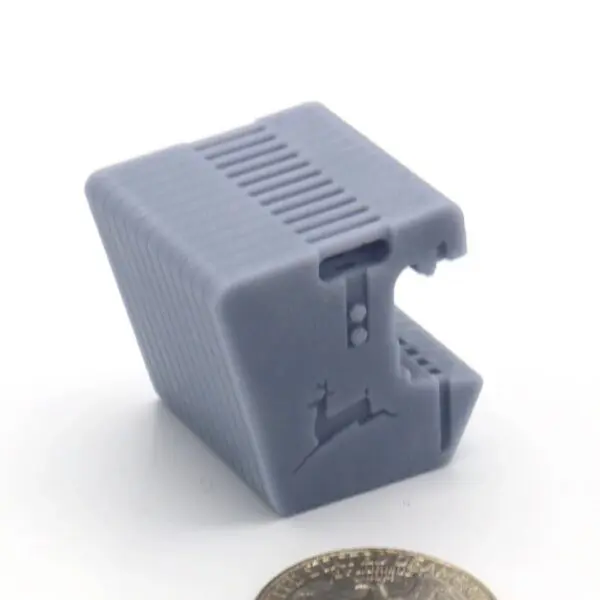 A small gray plastic device with a vented top and notches on the side.